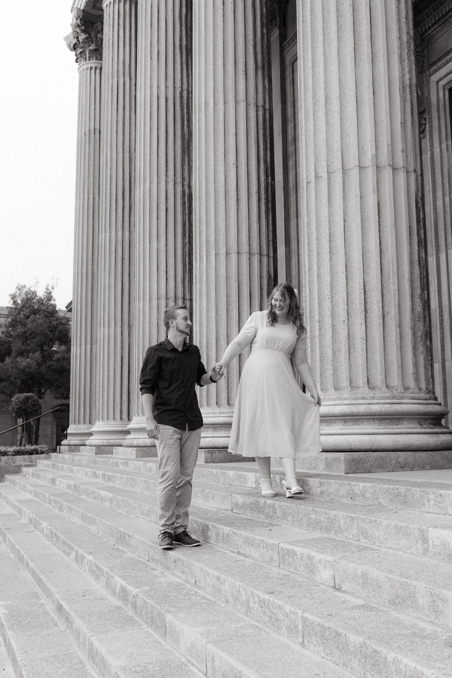 A couple descends stone steps between classical Greek columns in black and white photography.