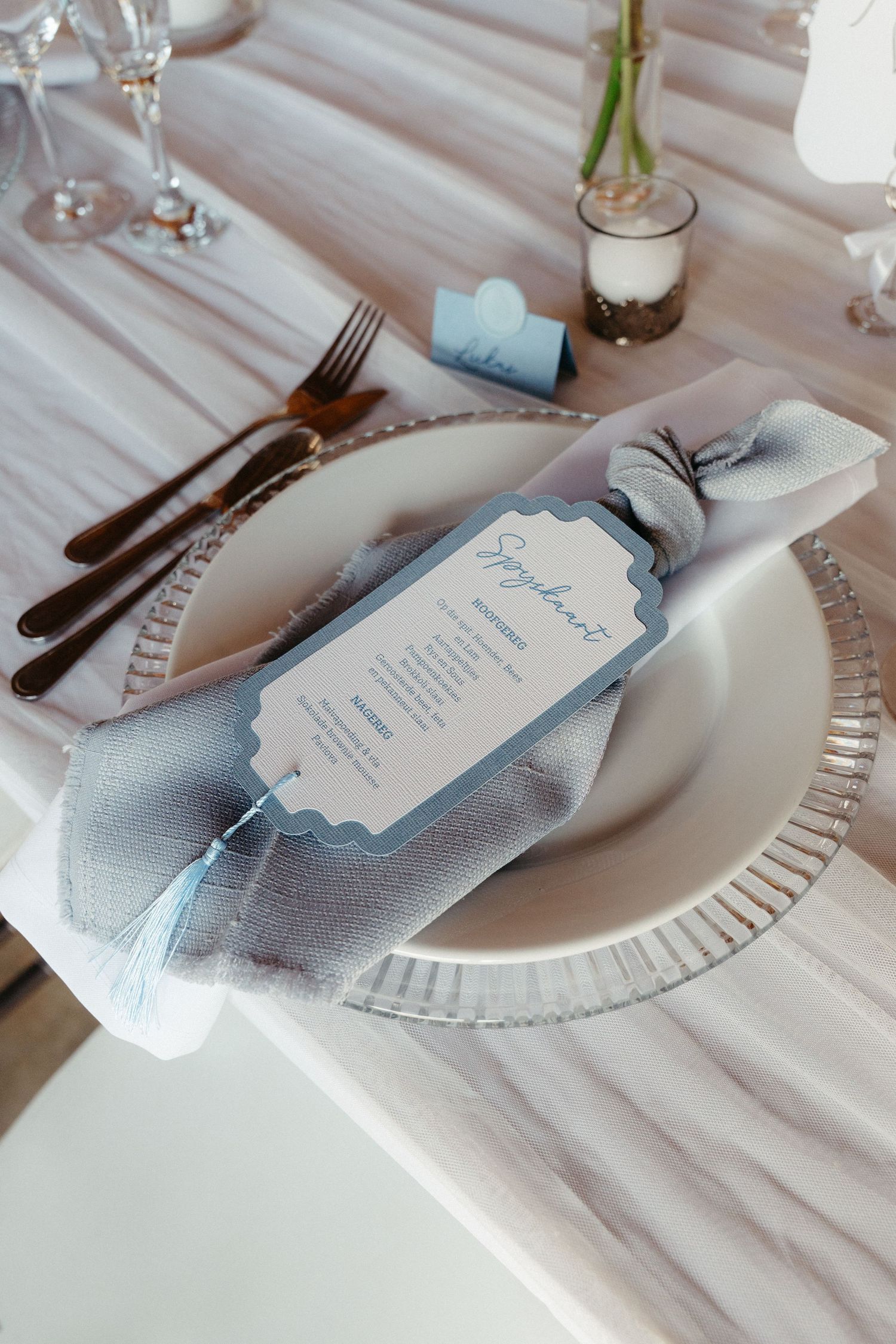 Elegant wedding table setting with white plates, silver cutlery and light blue menu cards on a textured white tablecloth.