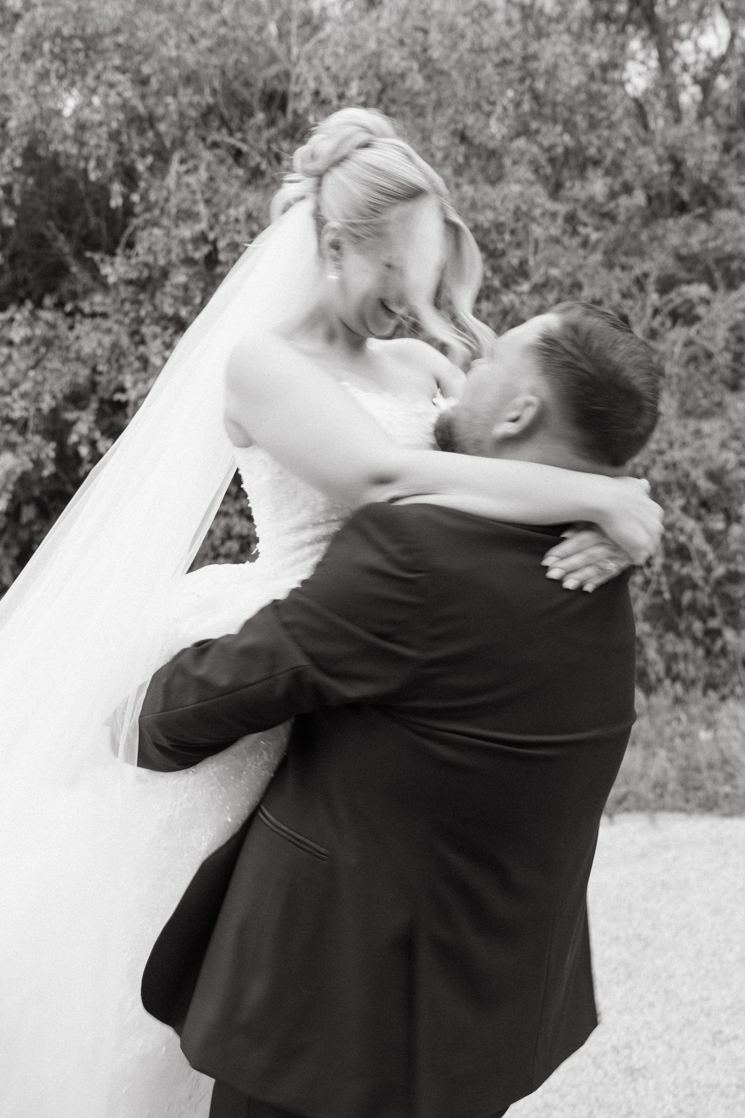 A couple in wedding attire embrace and spin joyfully during their outdoor celebration.