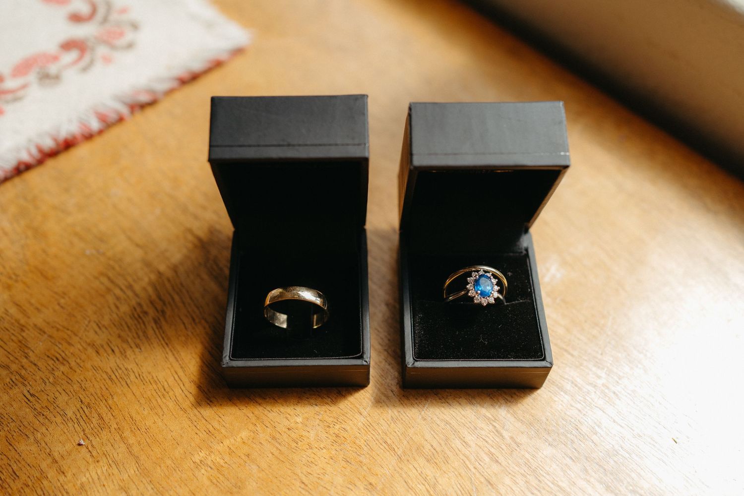 Two black jewelry boxes containing wedding rings displayed on a wooden surface.