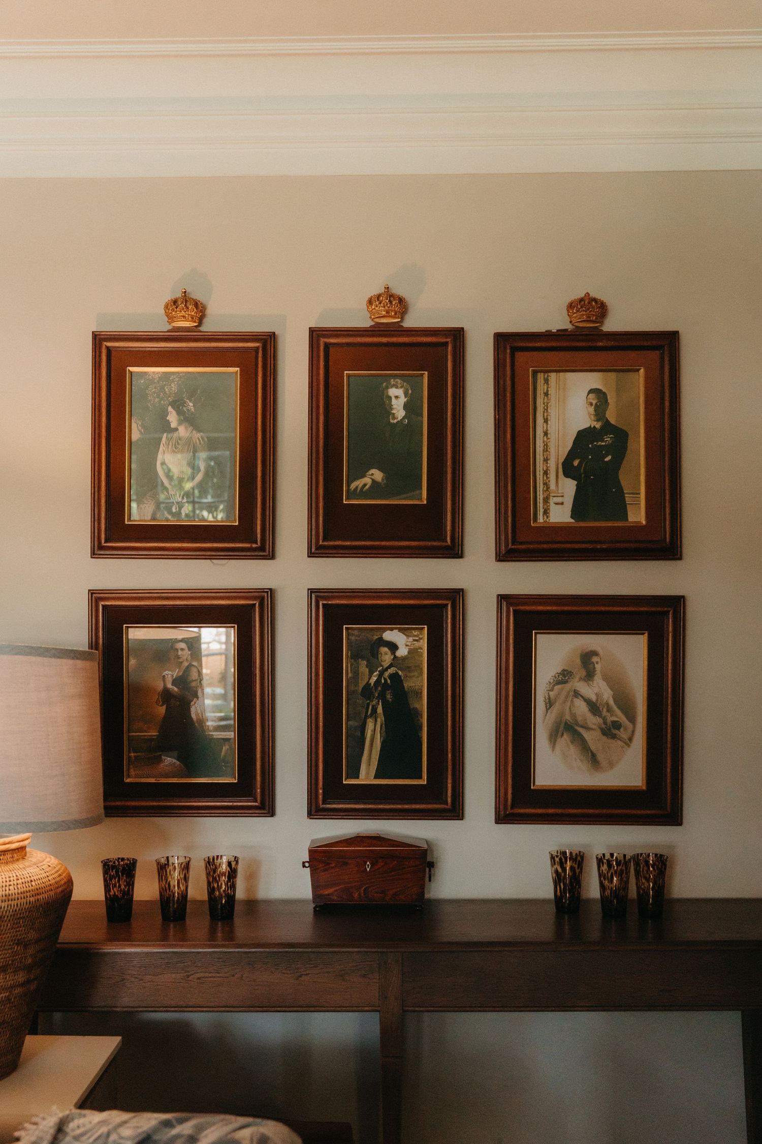 Six vintage portrait photographs in ornate dark wood frames with gold crown accents displayed on a beige wall above a wooden console.