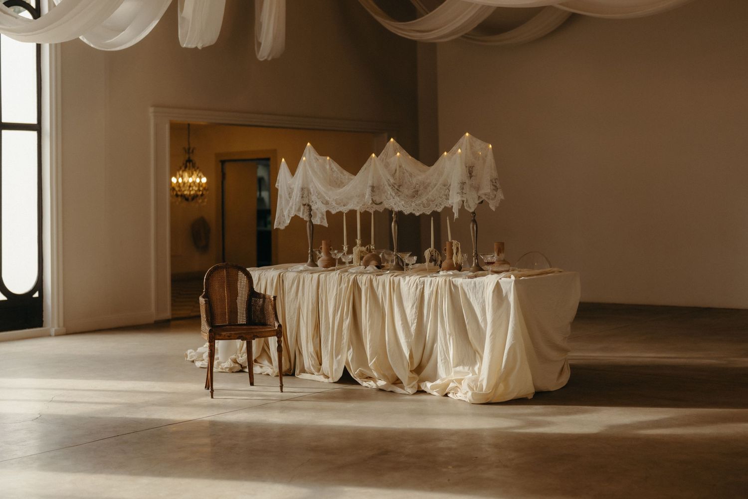 Elegant wedding sweetheart table with ivory draping and canopy in a sunlit ballroom.