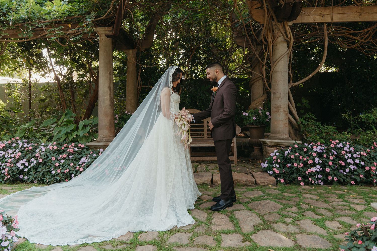 Bride and groom share a romantic first look in a lush garden wedding ceremony with floral arch and stone pathway.