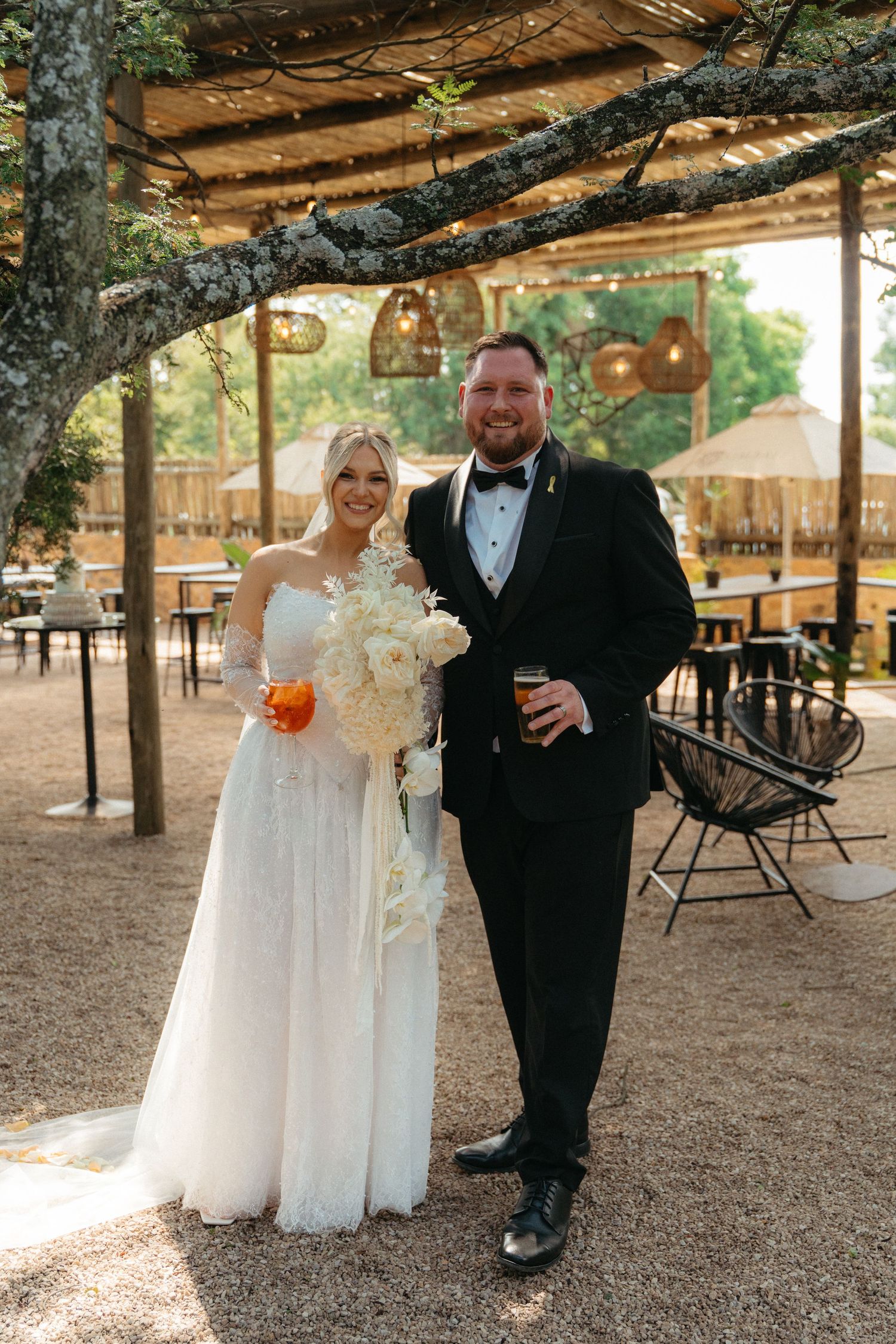 Couples enjoy drinks and celebrate under a rustic wooden pergola at an outdoor wedding reception.