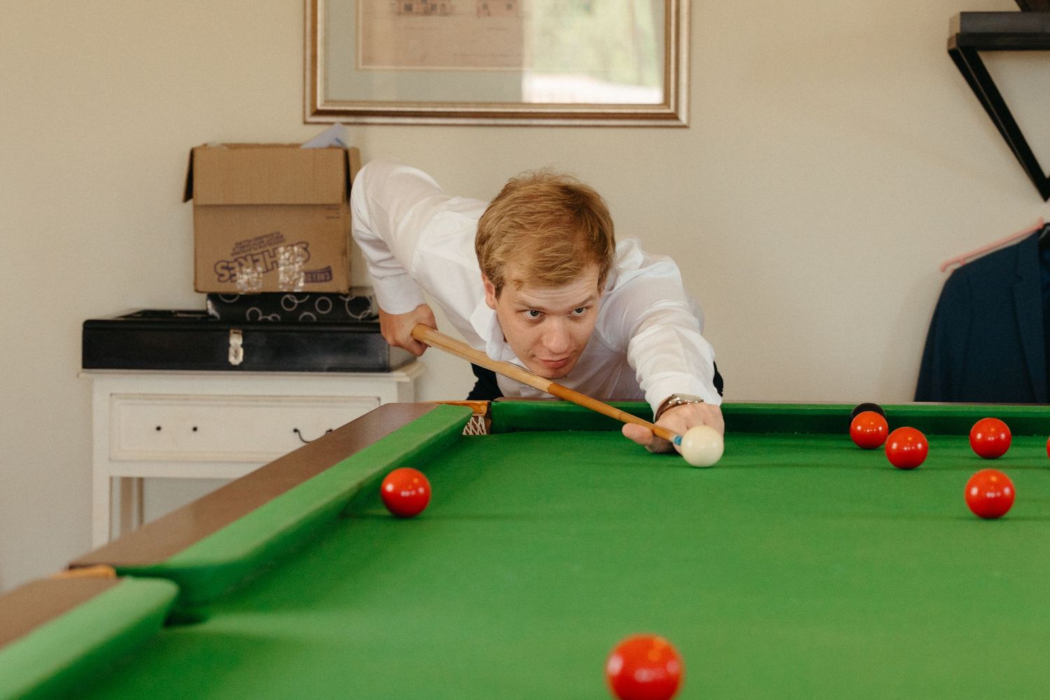 A player lines up a shot on a green snooker table while others watch the game in progress.