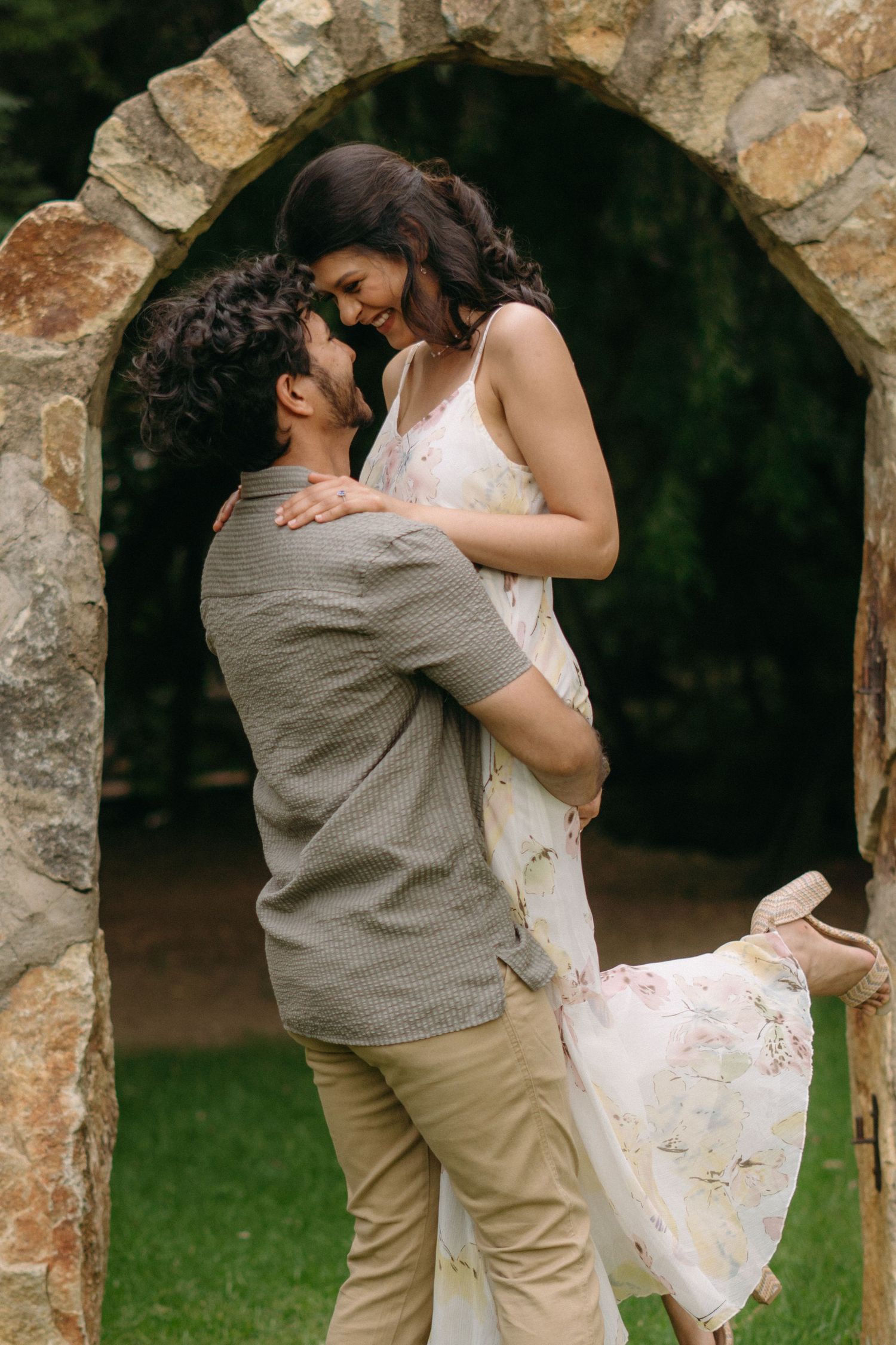 A playful romantic moment captured under a stone archway in a garden setting.