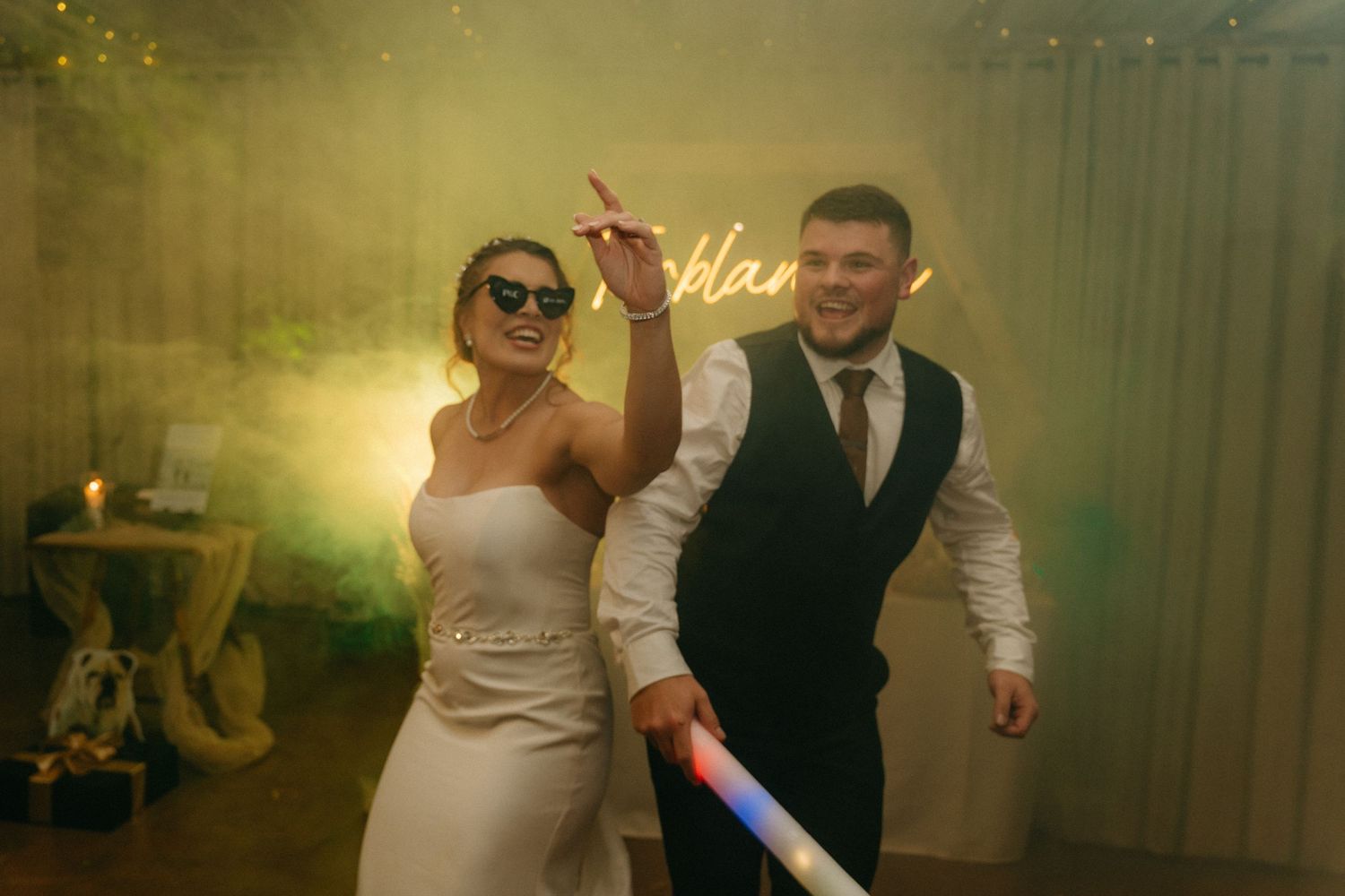 Wedding party dancing and celebrating at evening reception with ambient lighting.