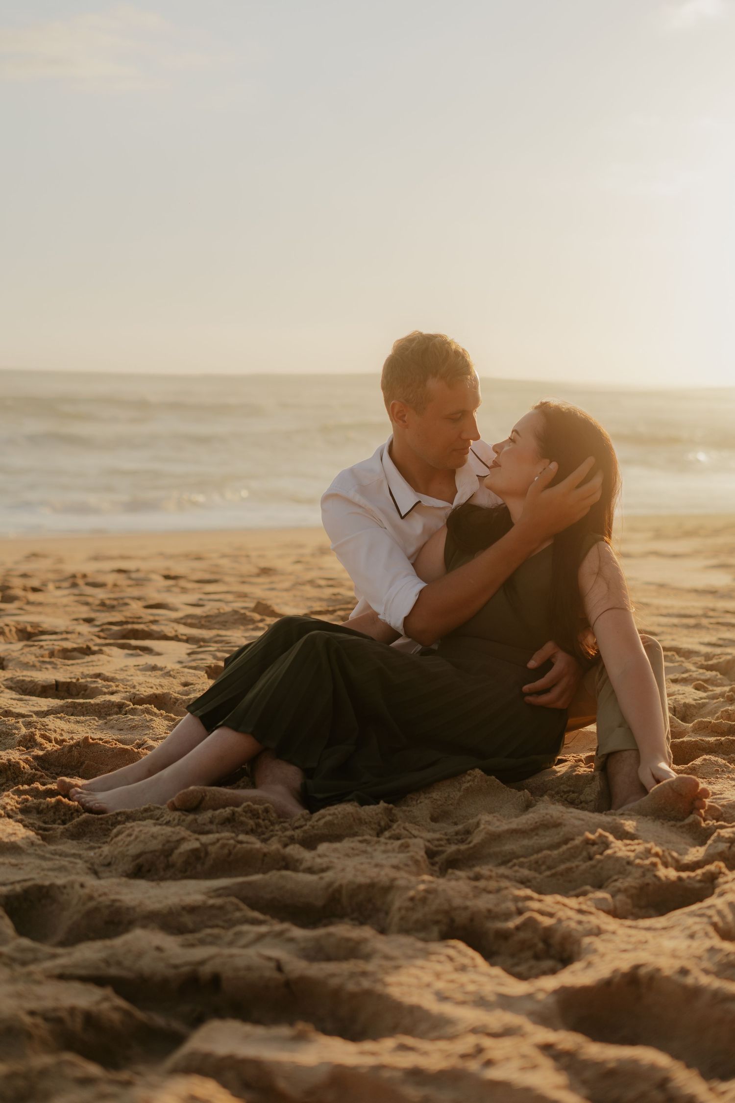 Romantic couple embraces on sandy beach at sunset in the Western Cape with golden light illuminating their intimate moment.