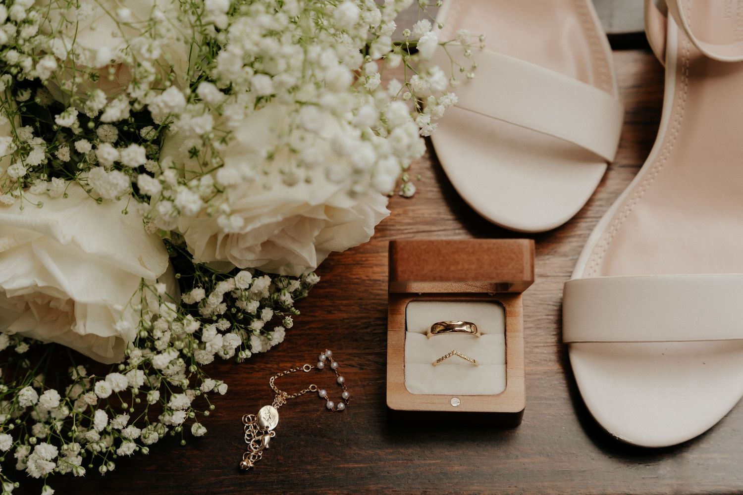 Wedding details including rings, baby's breath flowers, and decorative elements arranged on dark wood surface.