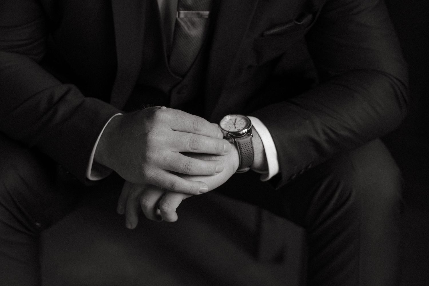 Close-up details of groomsmen in black suits showing hands and accessories.