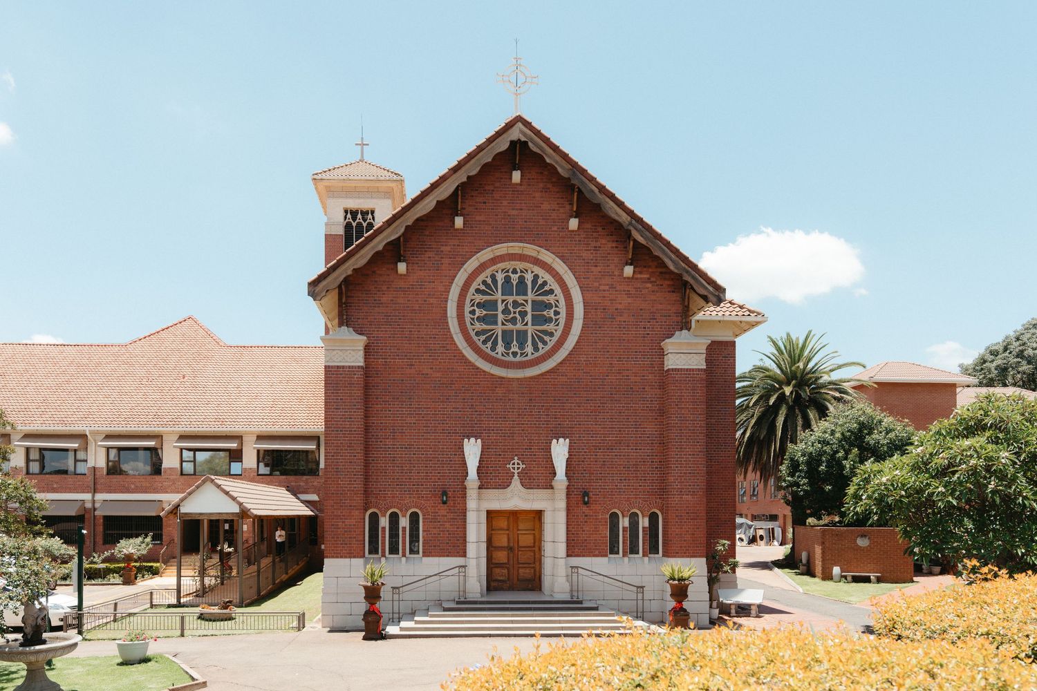 A panoramic view of a Nazareth House Chapel with a cross on top and palm trees in the surrounding landscape of Pretoria