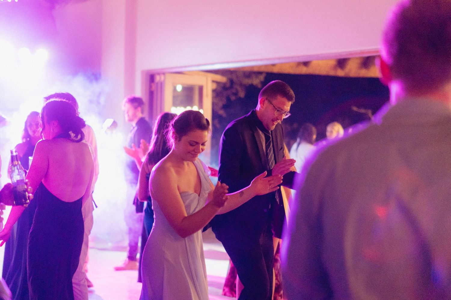 Party guests dancing under purple mood lighting at a festive indoor celebration.
