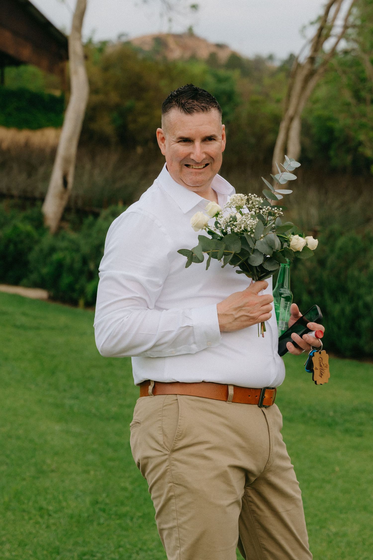 Groomsmen in khaki pants and white shirts hold floral bouquets in a garden setting.