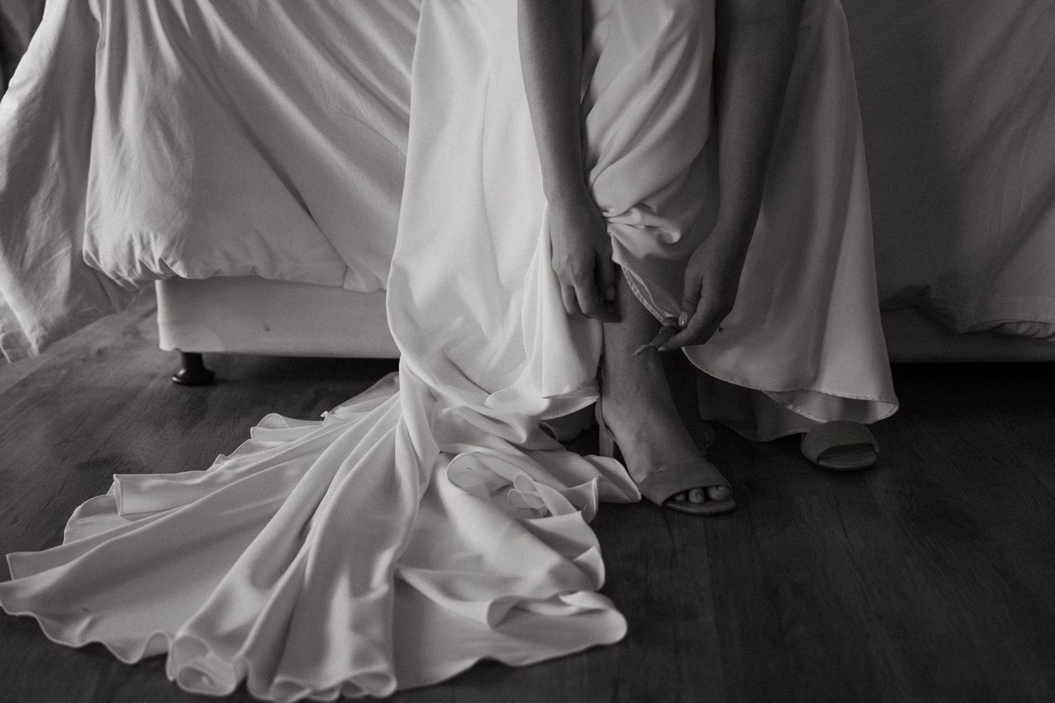 Black and white detail shot of a wedding dress hem and bare feet on wooden floor.