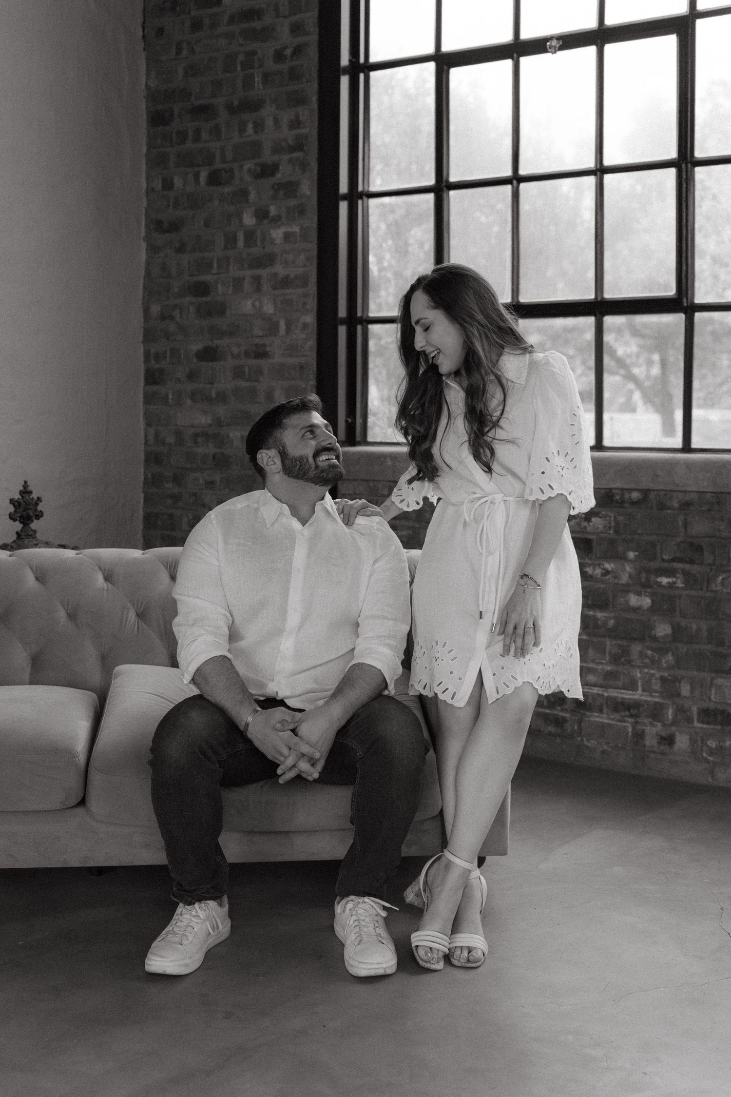 Black and white photo series showing a couple sitting on a white couch in an industrial loft space with brick walls.