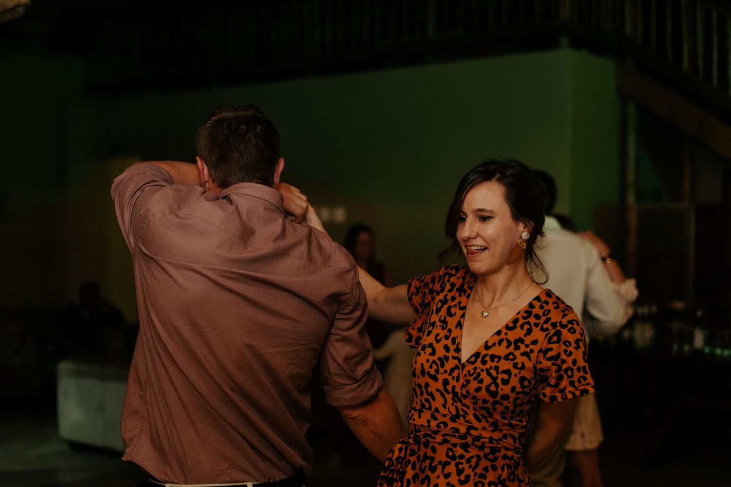 Wedding guests dancing and celebrating at an evening reception with warm lighting.