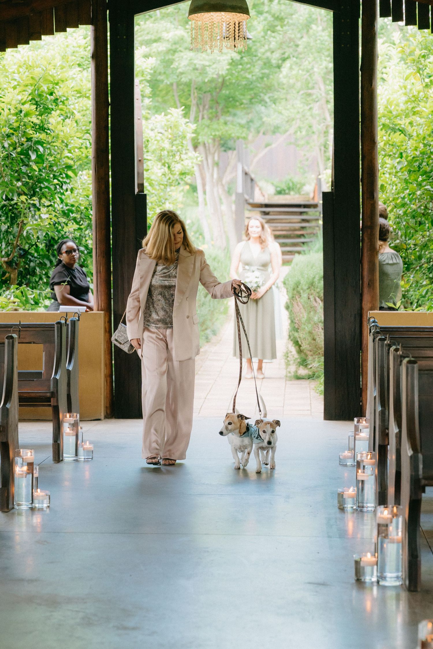 Wedding party members walk through a covered outdoor venue decorated with candles and natural light.