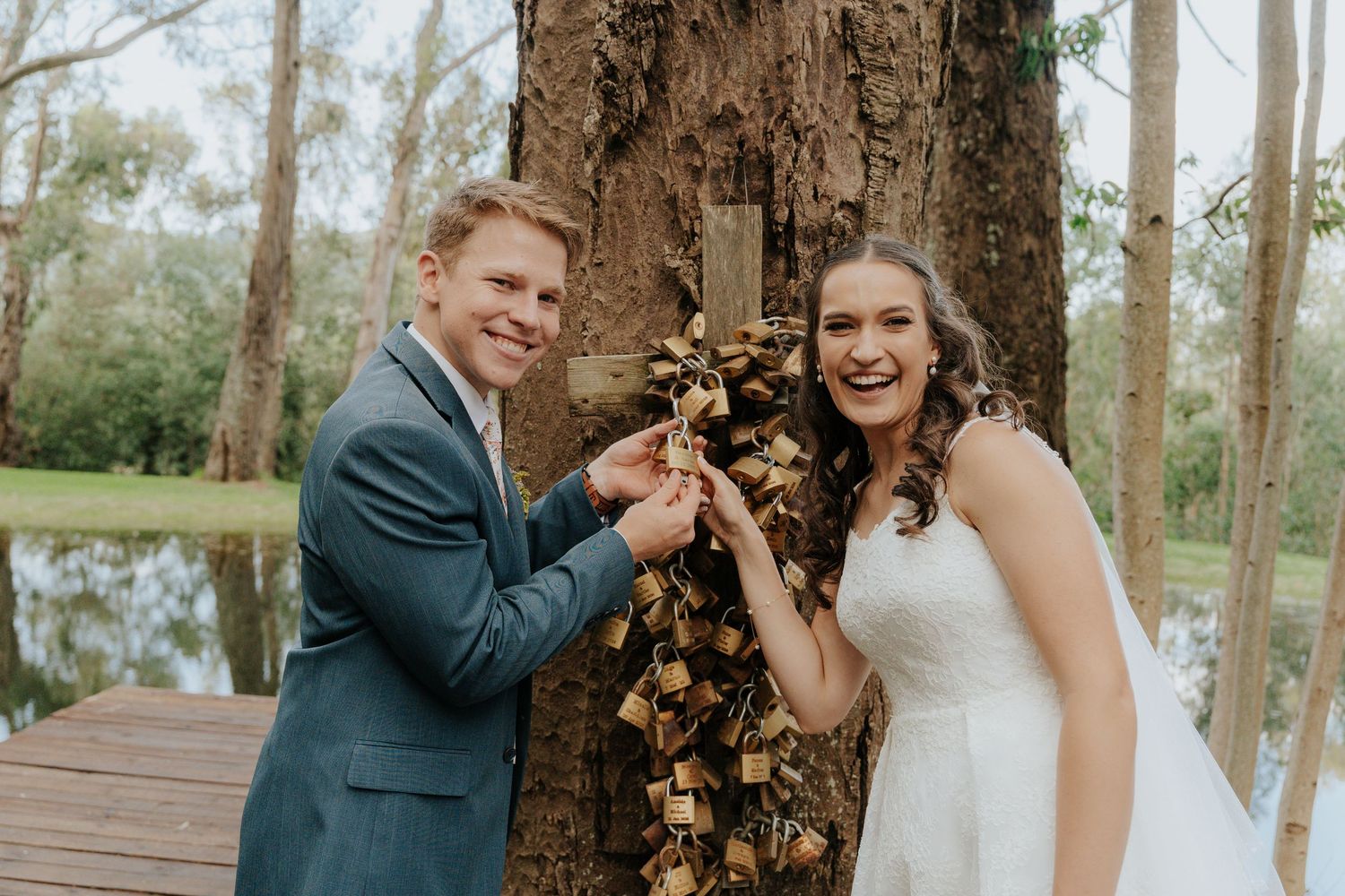 A couple in wedding attire poses together in front of tall trees during their outdoor forest ceremony.