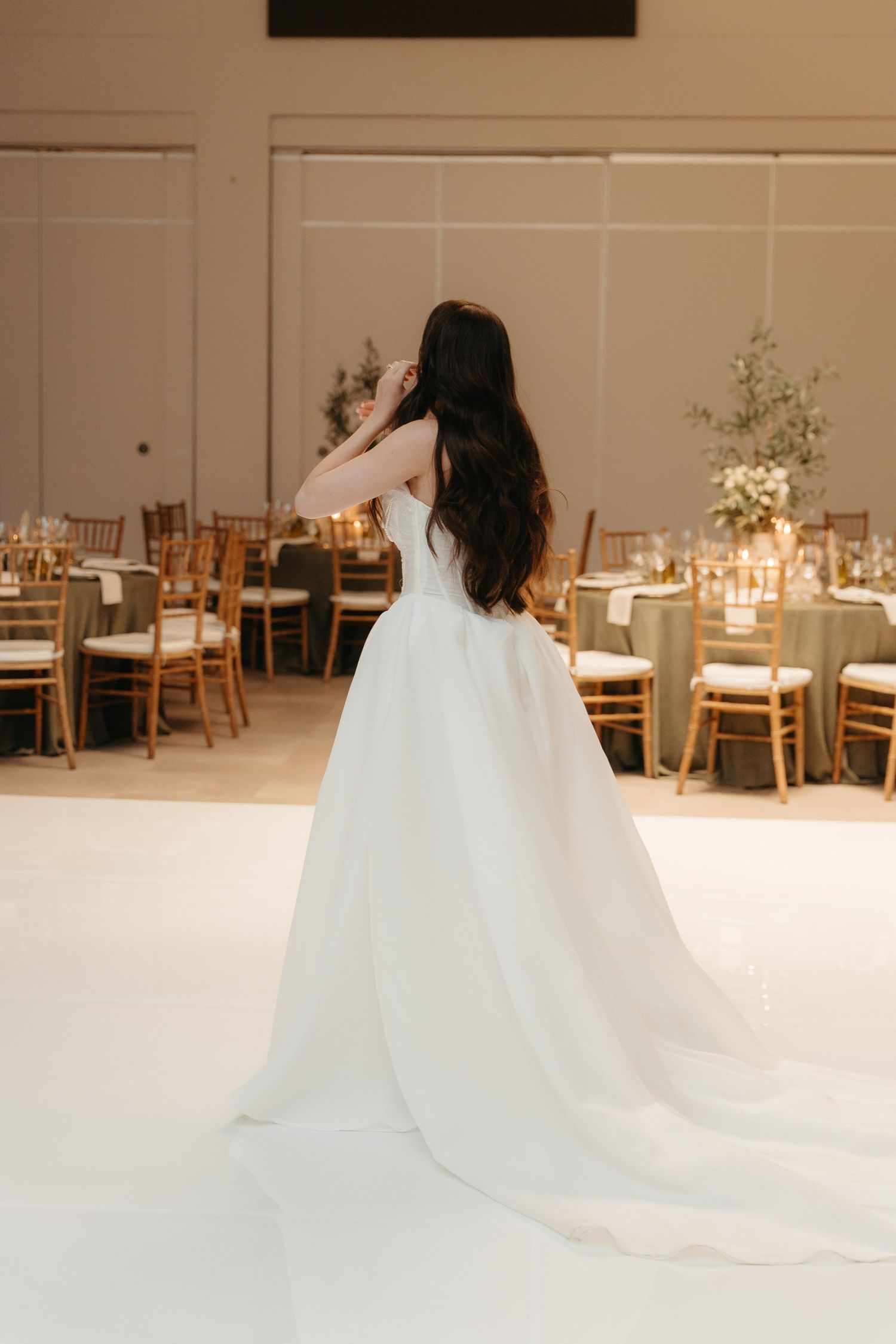 Bride in white ballgown with long train stands on dance floor in elegantly decorated wedding reception venue.