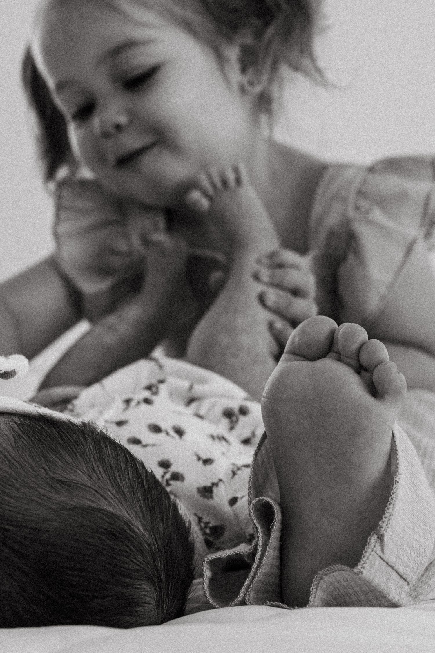 Toddler playing with newborn baby feet in lifestyle family session in Mesa, AZ