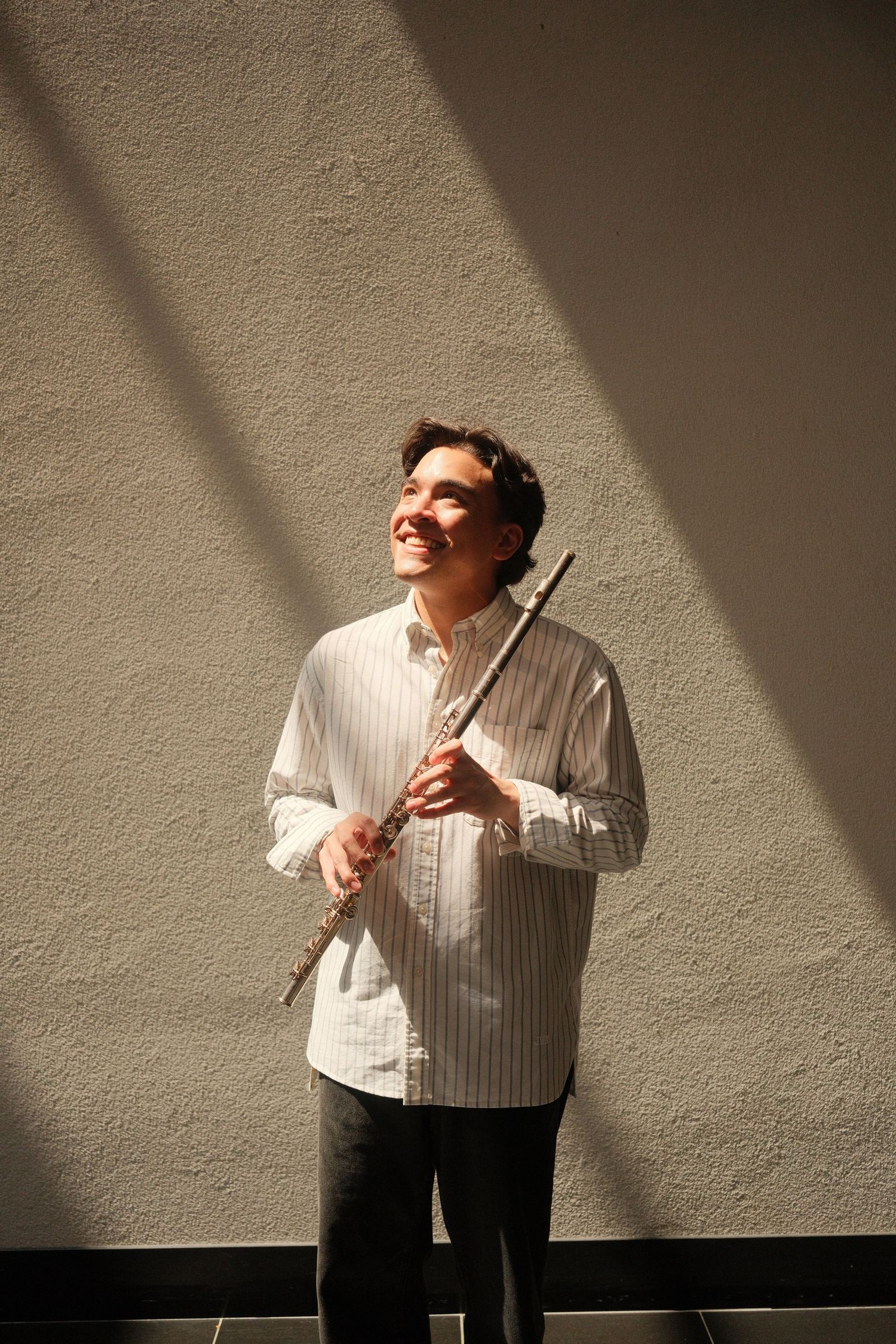Dramatic indoor portrait of a man holding a flute with strong light and shadow contrast.