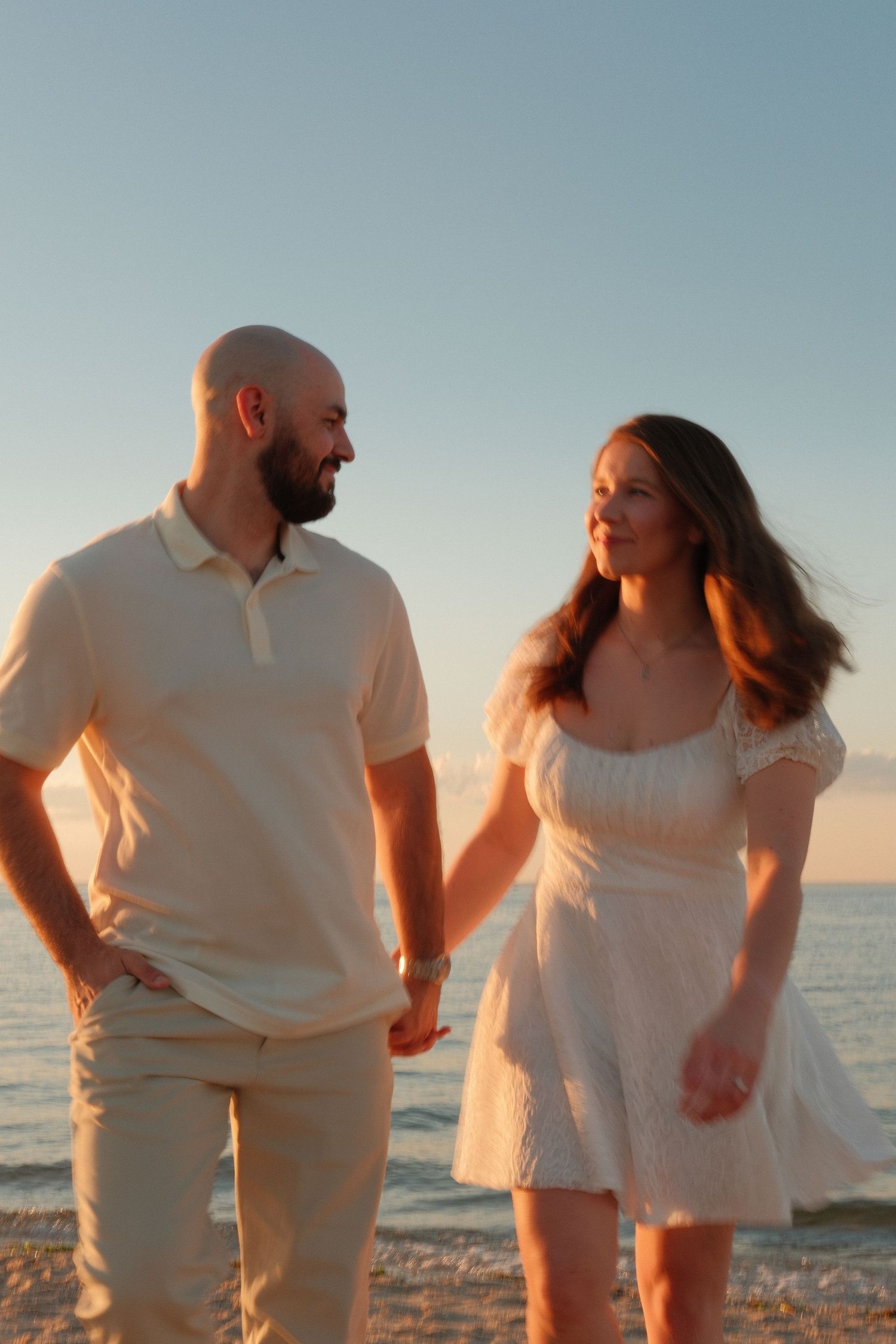 Couple holding hands during a golden hour beach engagement photoshoot.