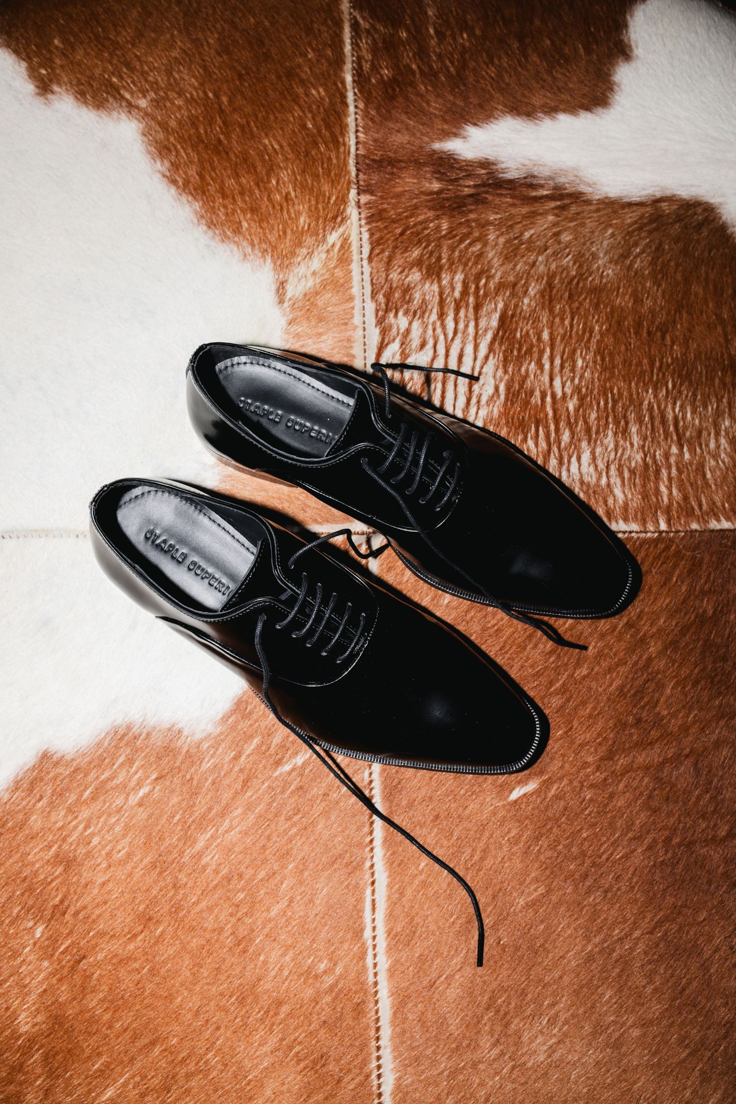 Black lace-up oxford dress shoes on a brown and white cowhide rug.