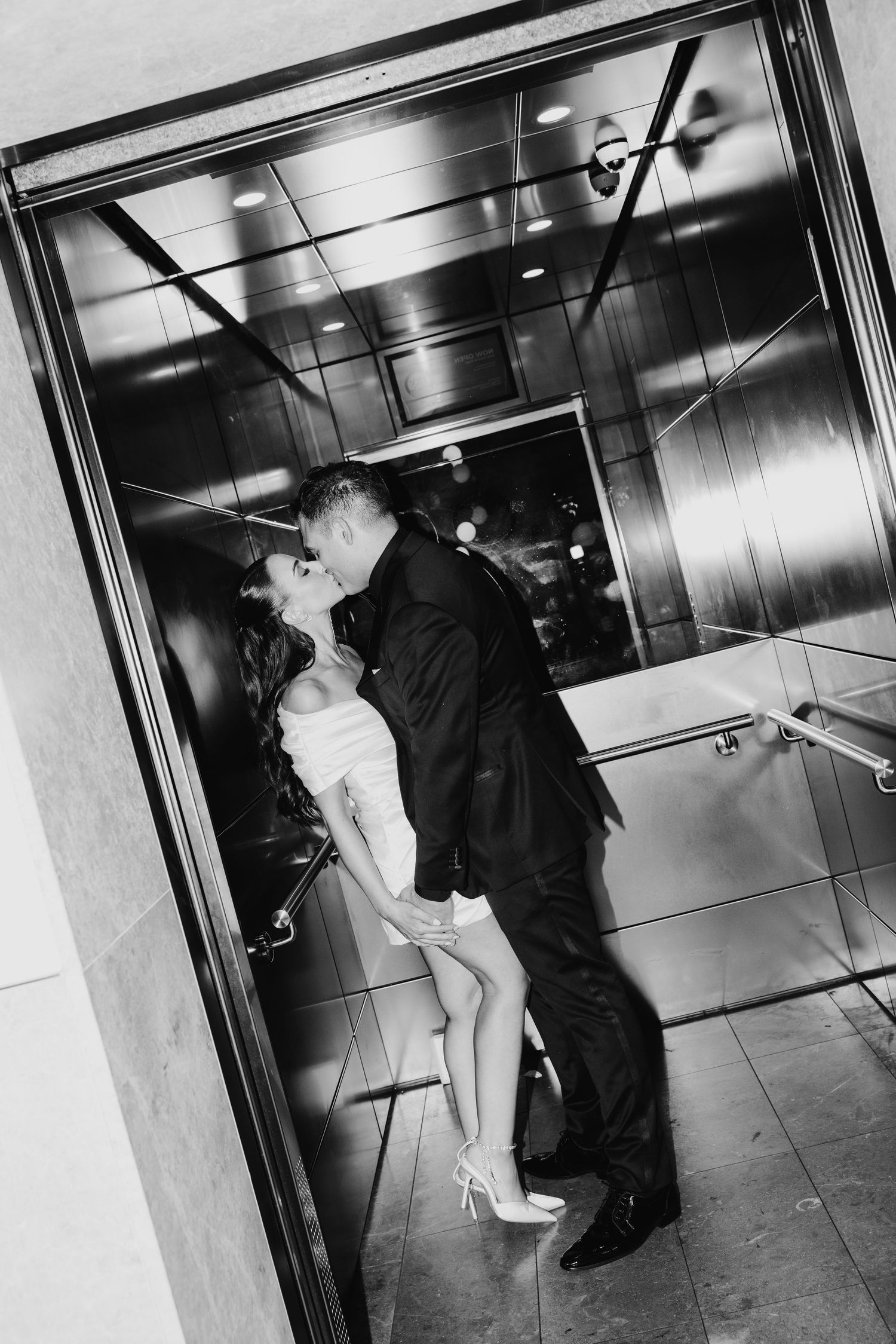 Black and white photo of bride and groom kissing romantically inside a mirrored elevator.