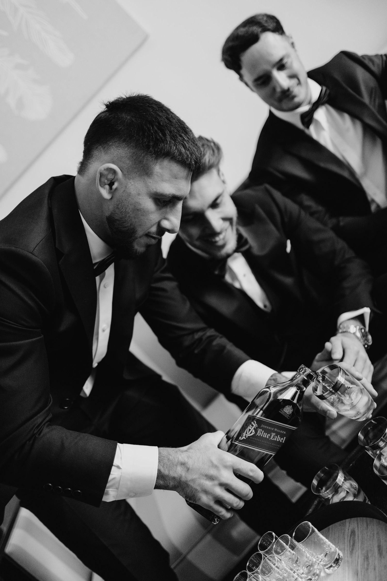 Three men in tuxedos pour Johnnie Walker Black Label whiskey into glasses in a black and white photo.