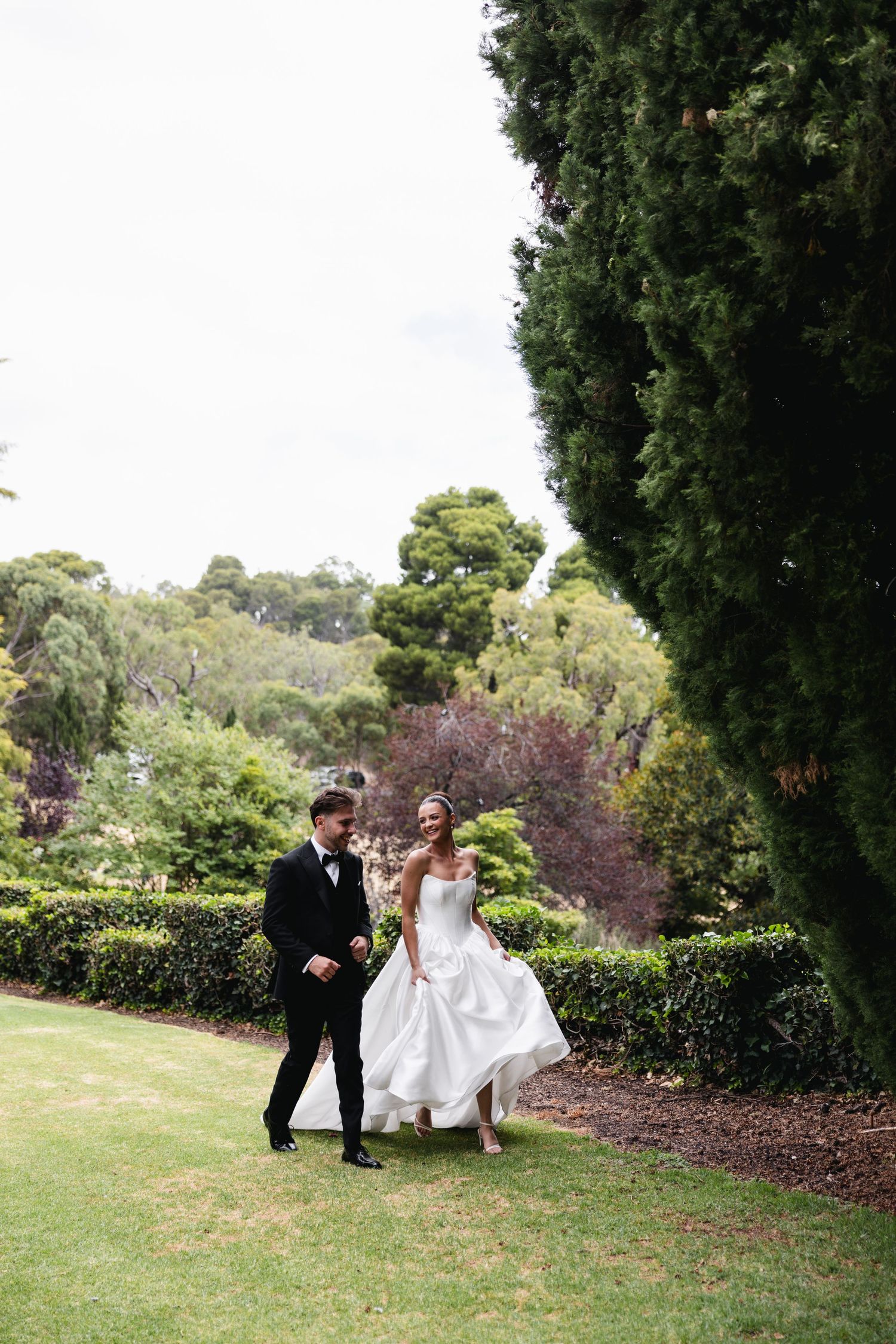 Bride and groom walking hand in hand through lush green garden grounds on their wedding day.