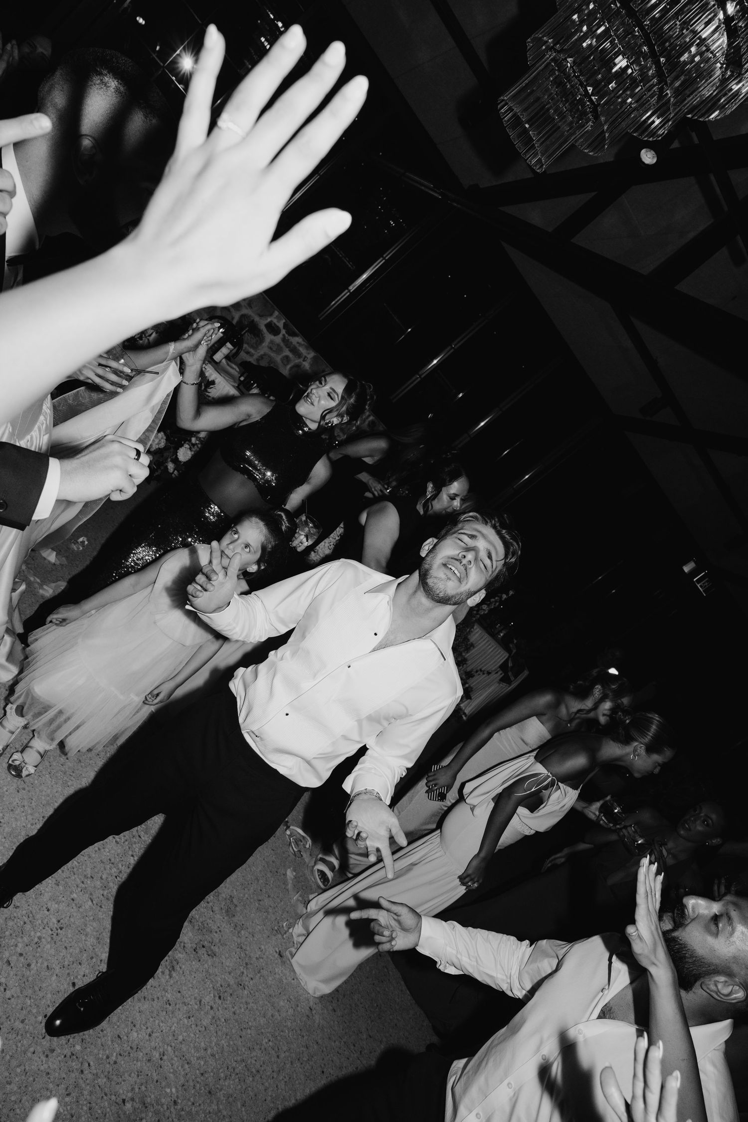 Black and white photo of guests dancing at a lively wedding reception party on the dance floor.