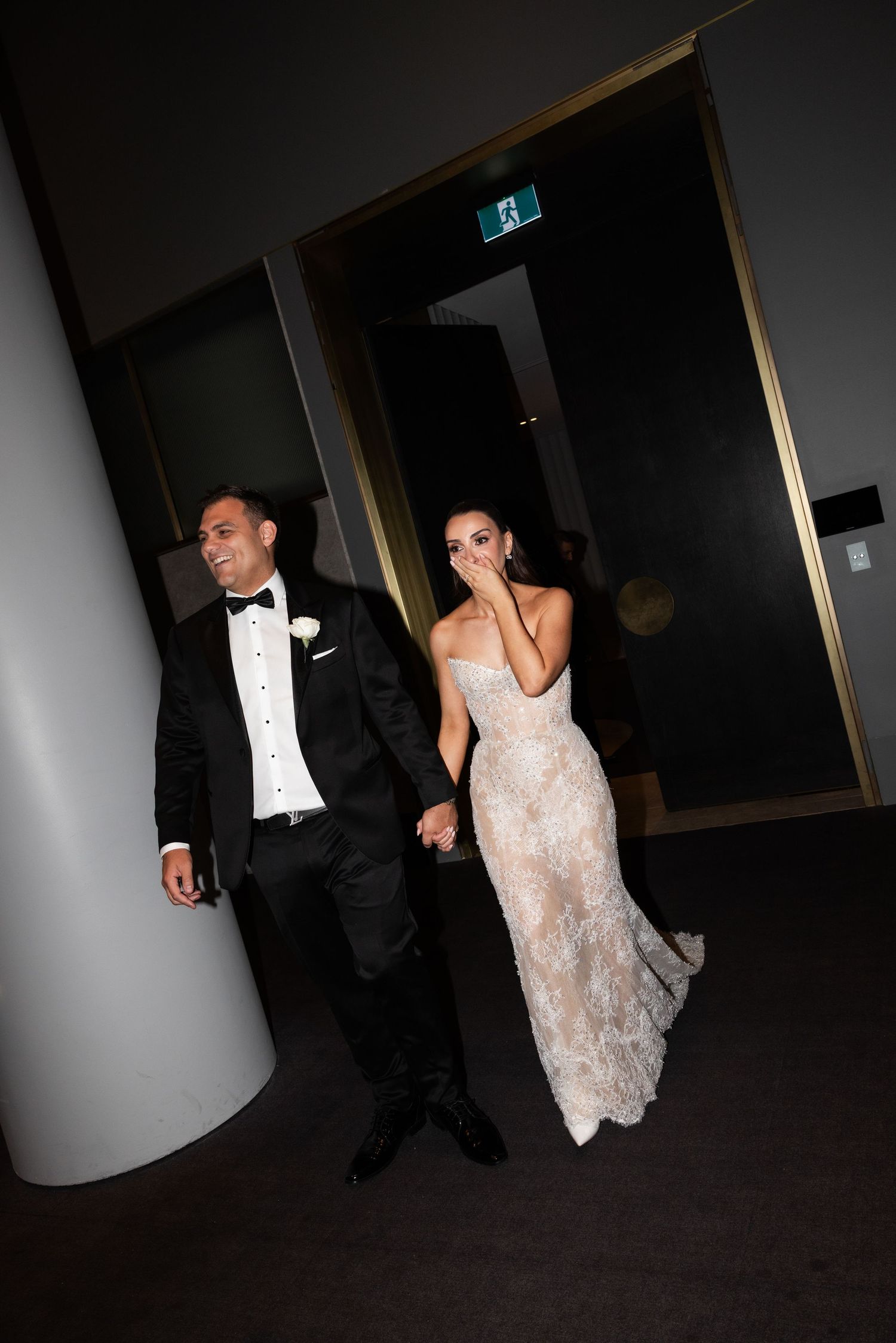 Bride covering mouth in excitement as groom leads her into reception venue.