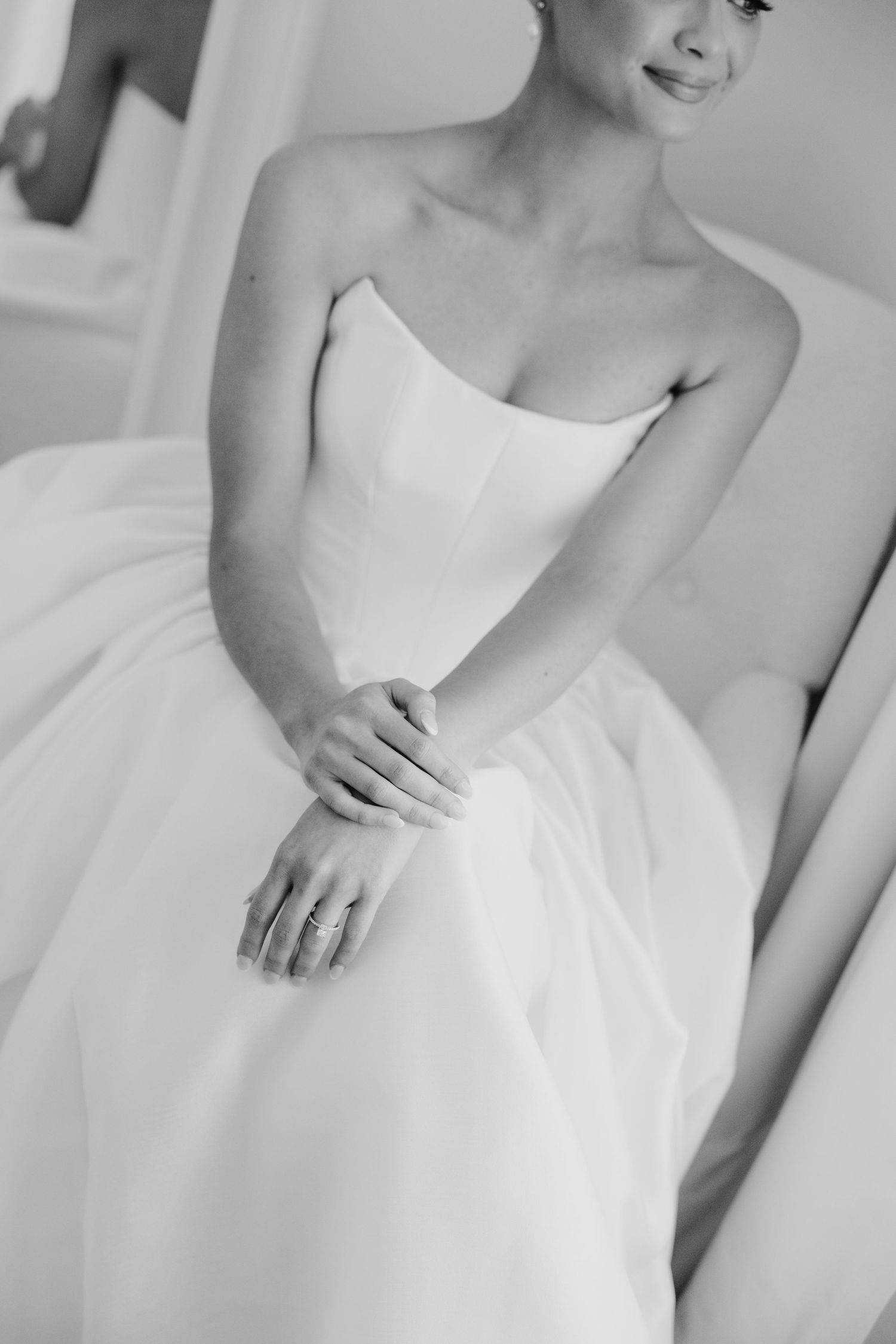 Black and white photo of a bride in a strapless ball gown, hands folded gracefully, wearing an engagement ring.