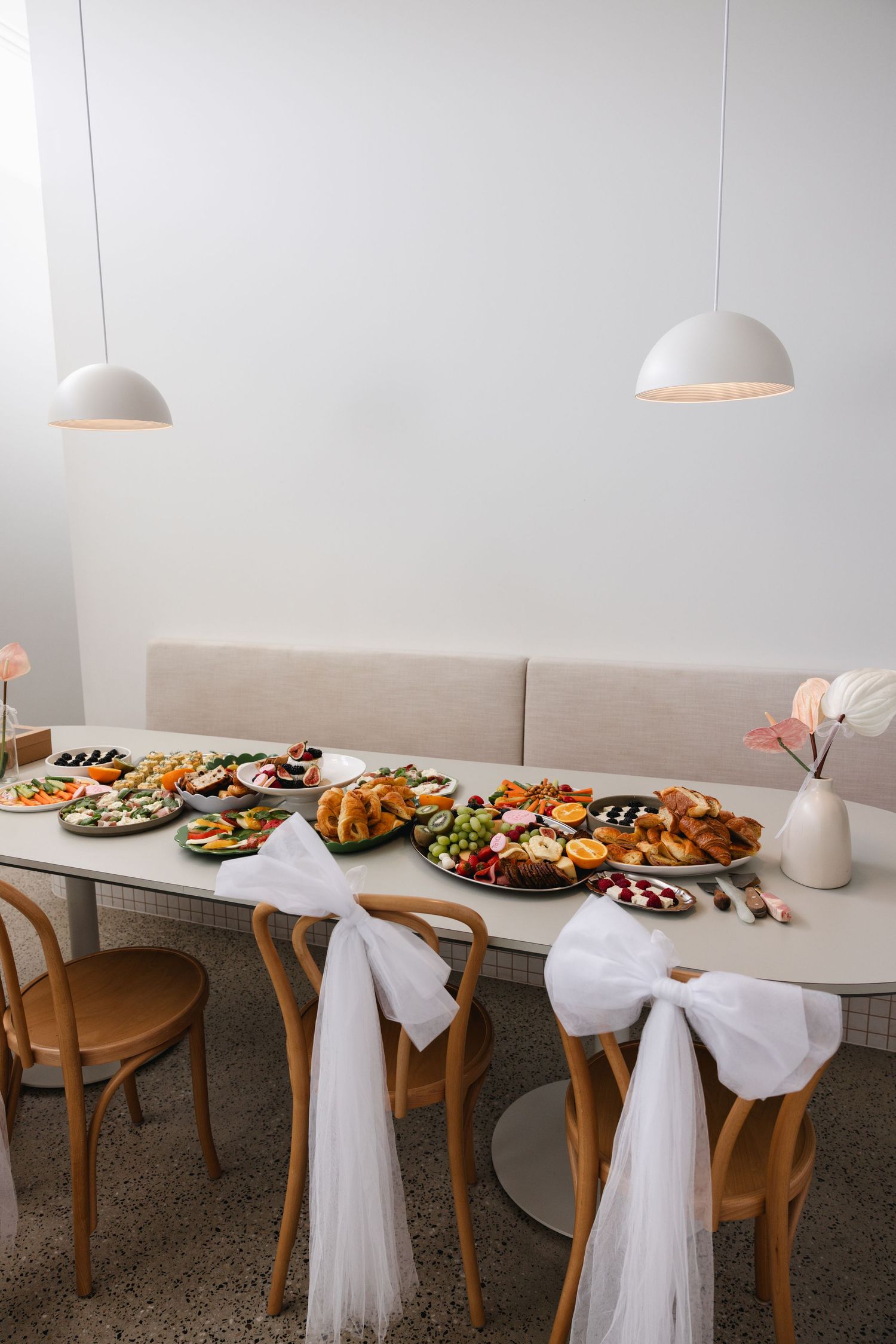 Elegant wedding reception table adorned with lavish food platters, white bow chairs, and soft pendant lighting.