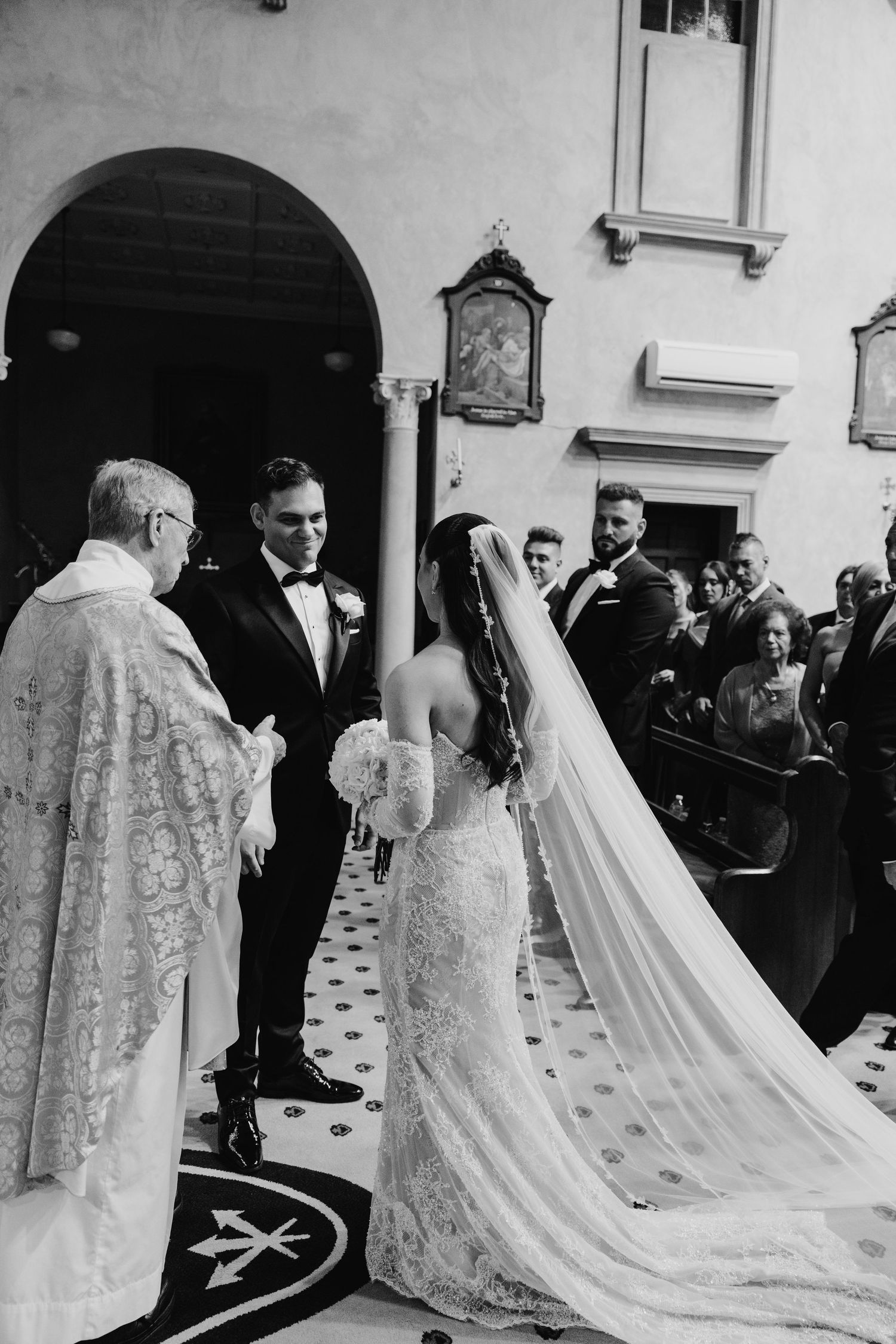 Bride and groom exchange vows with priest at elegant church wedding ceremony in black and white.