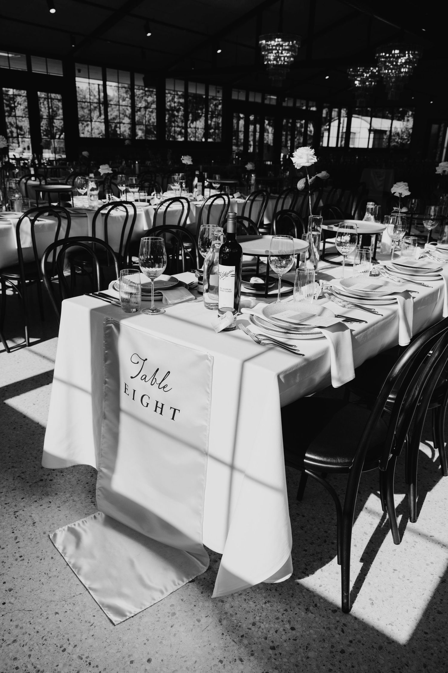 Black and white photo of an elegant wedding reception table setup with white linens and a Table Eight sign.