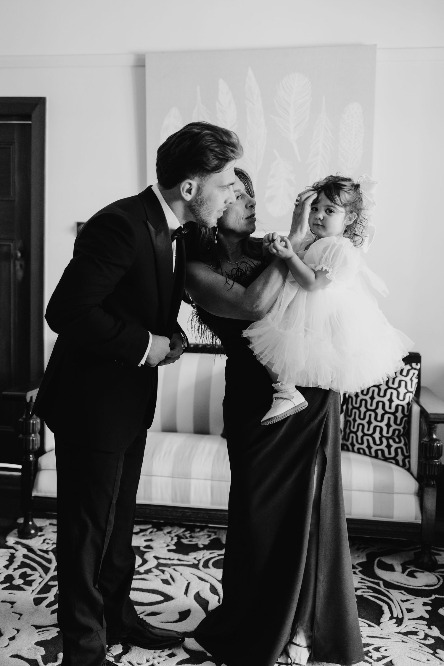 Black and white photo of a groom in tuxedo and woman in gown holding a little girl in white tutu dress.