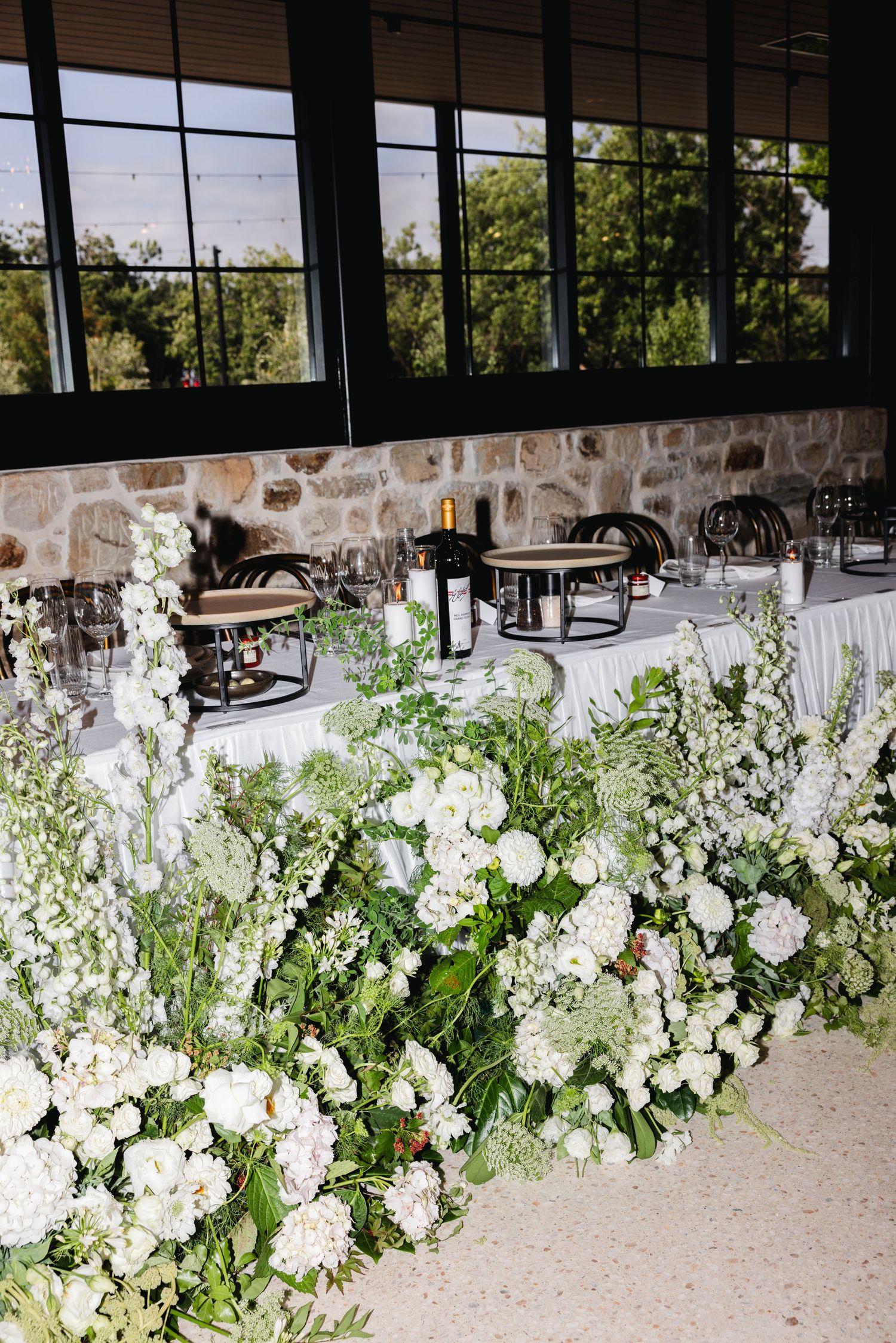 Elegant wedding reception table adorned with lush white floral arrangements and greenery in a rustic stone venue.