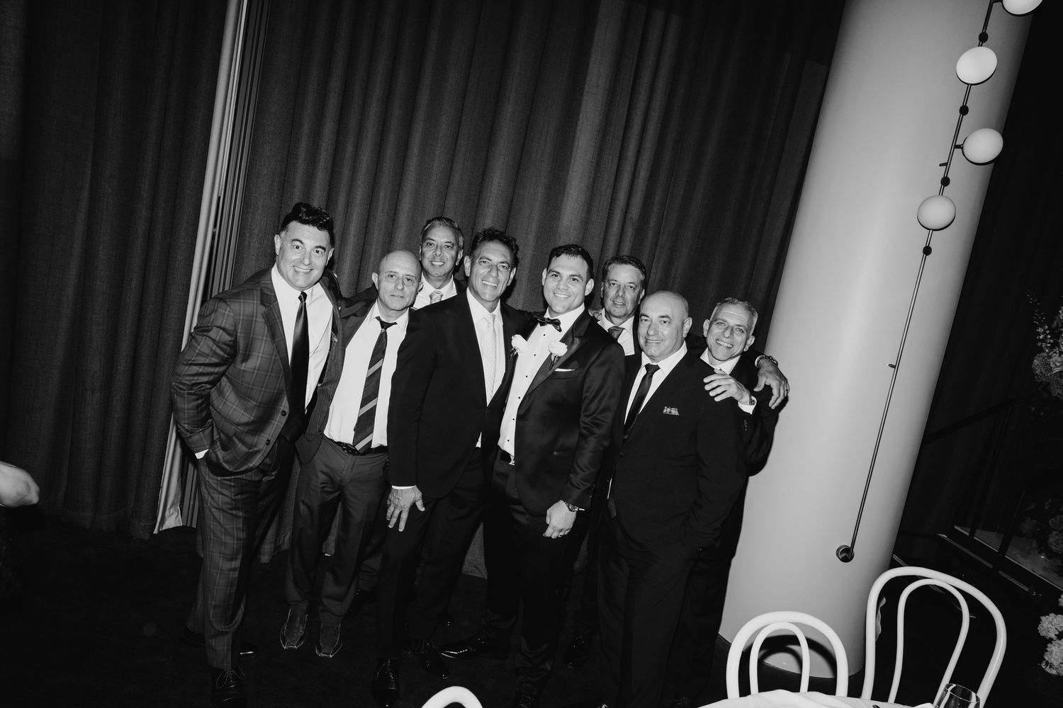 Black and white photo of a group of men in suits and tuxedos posing together at a formal event.