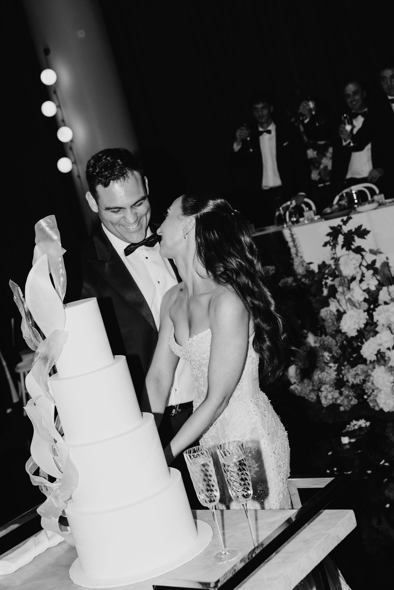 Bride and groom cutting tiered white wedding cake at evening reception.