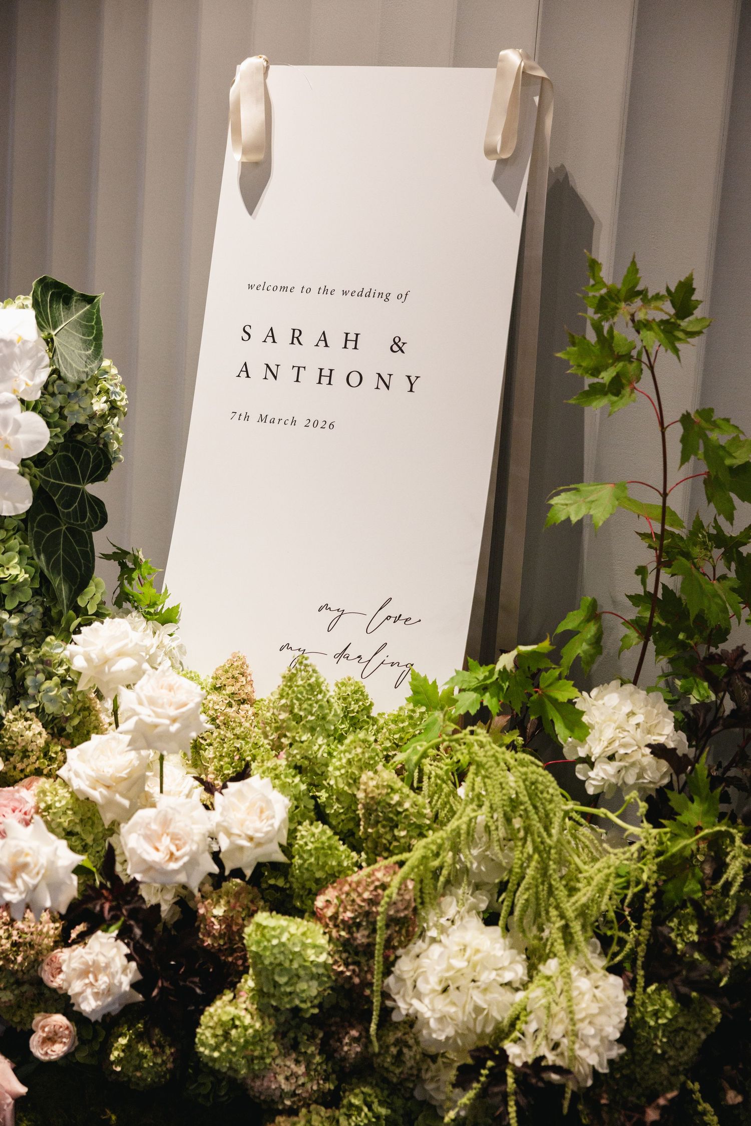Elegant wedding welcome sign for Sarah & Anthony surrounded by lush white hydrangeas and green foliage arrangements.