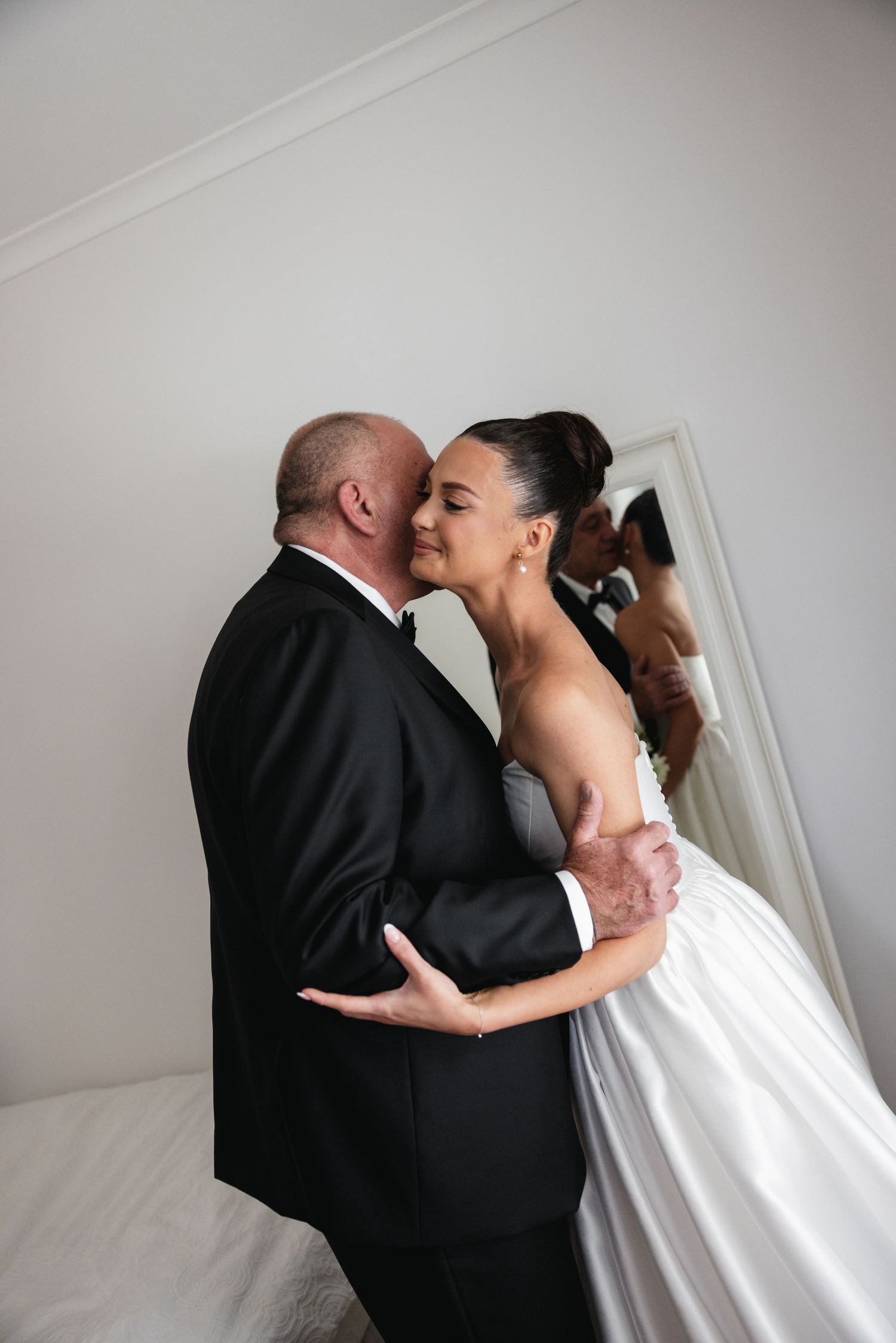 Bride and groom share a romantic embrace in wedding attire, reflected in a mirror behind them.