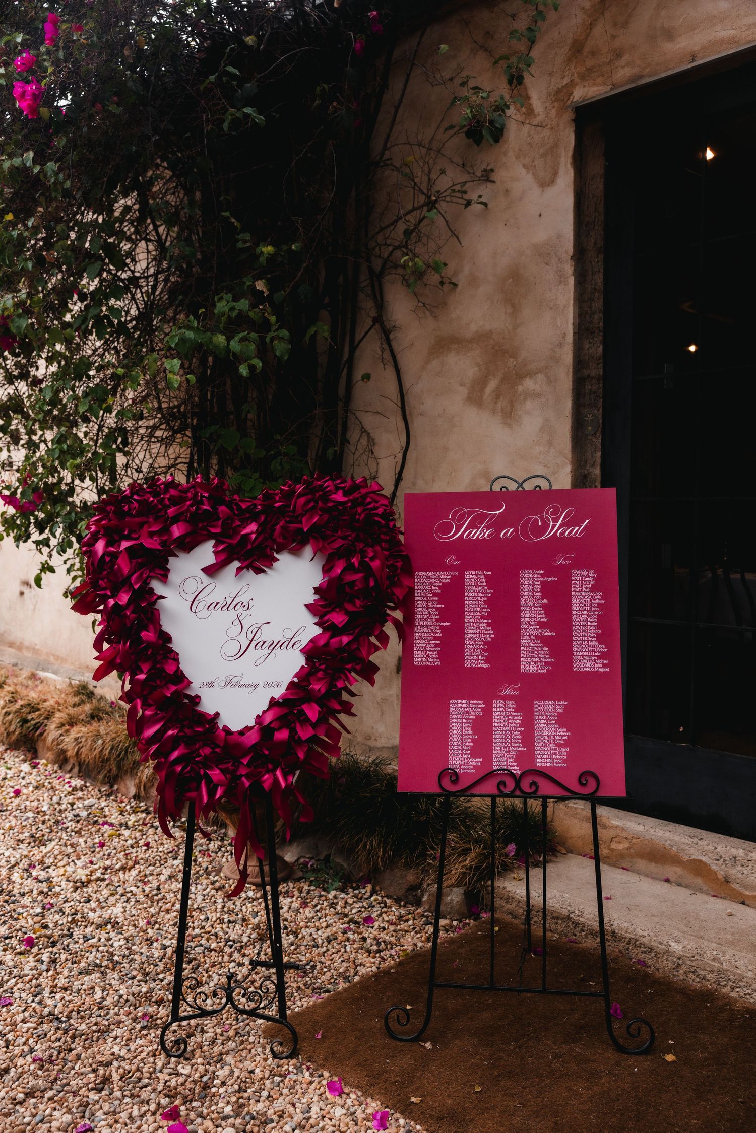 Heart-shaped floral wreath wedding seating chart display with hot pink flowers and signage.