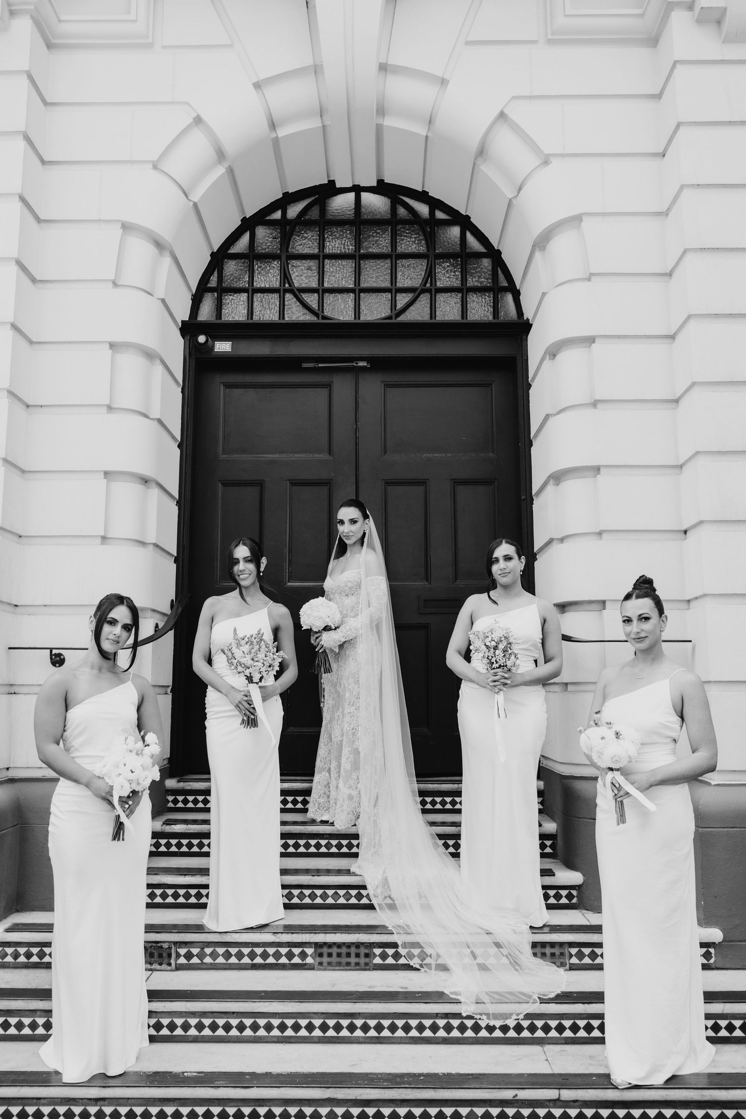Black and white photo of bride with four bridesmaids in white gowns on ornate building steps.