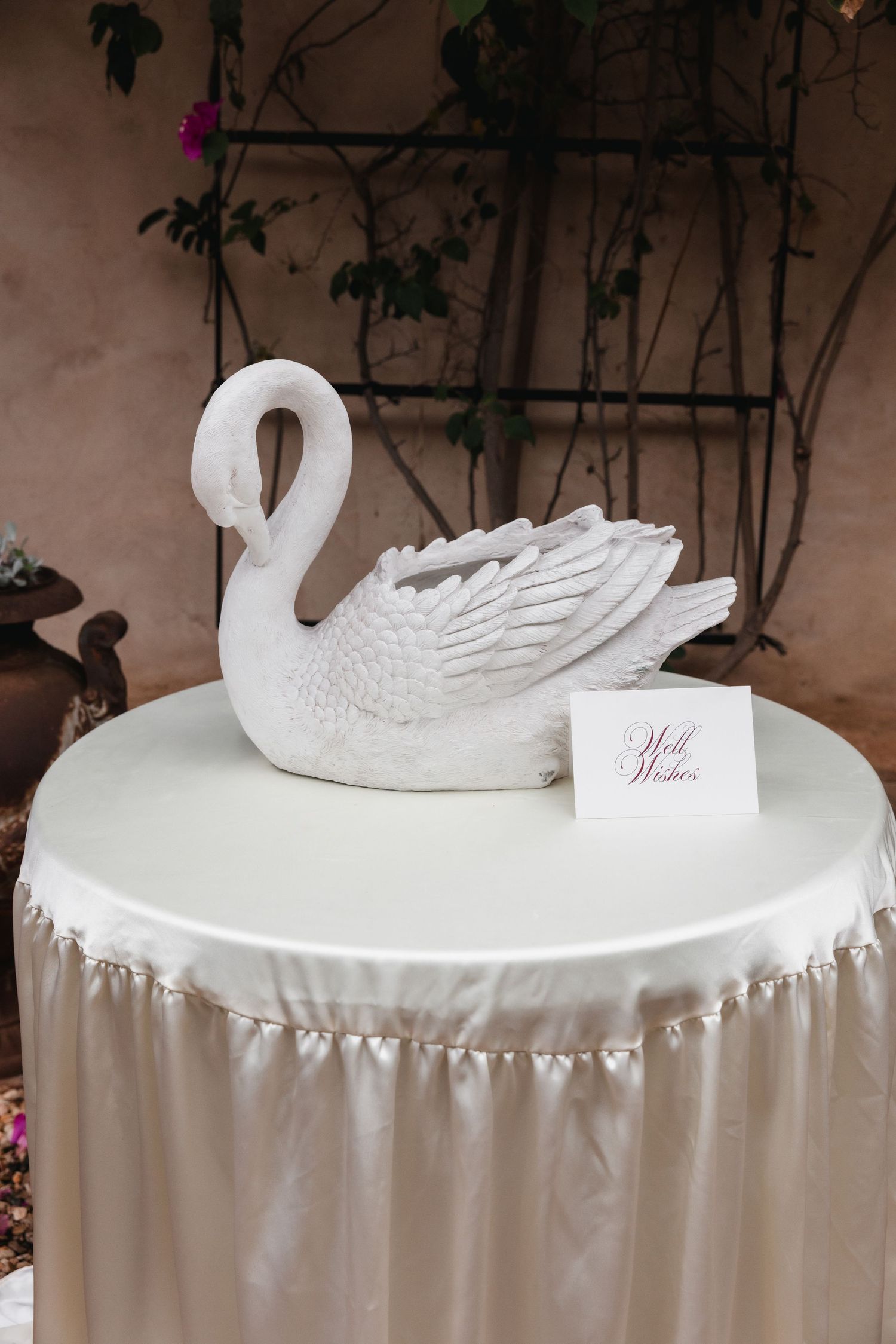 White swan sculpture centerpiece on a satin-draped table with a Well Wishes card at an elegant wedding reception.