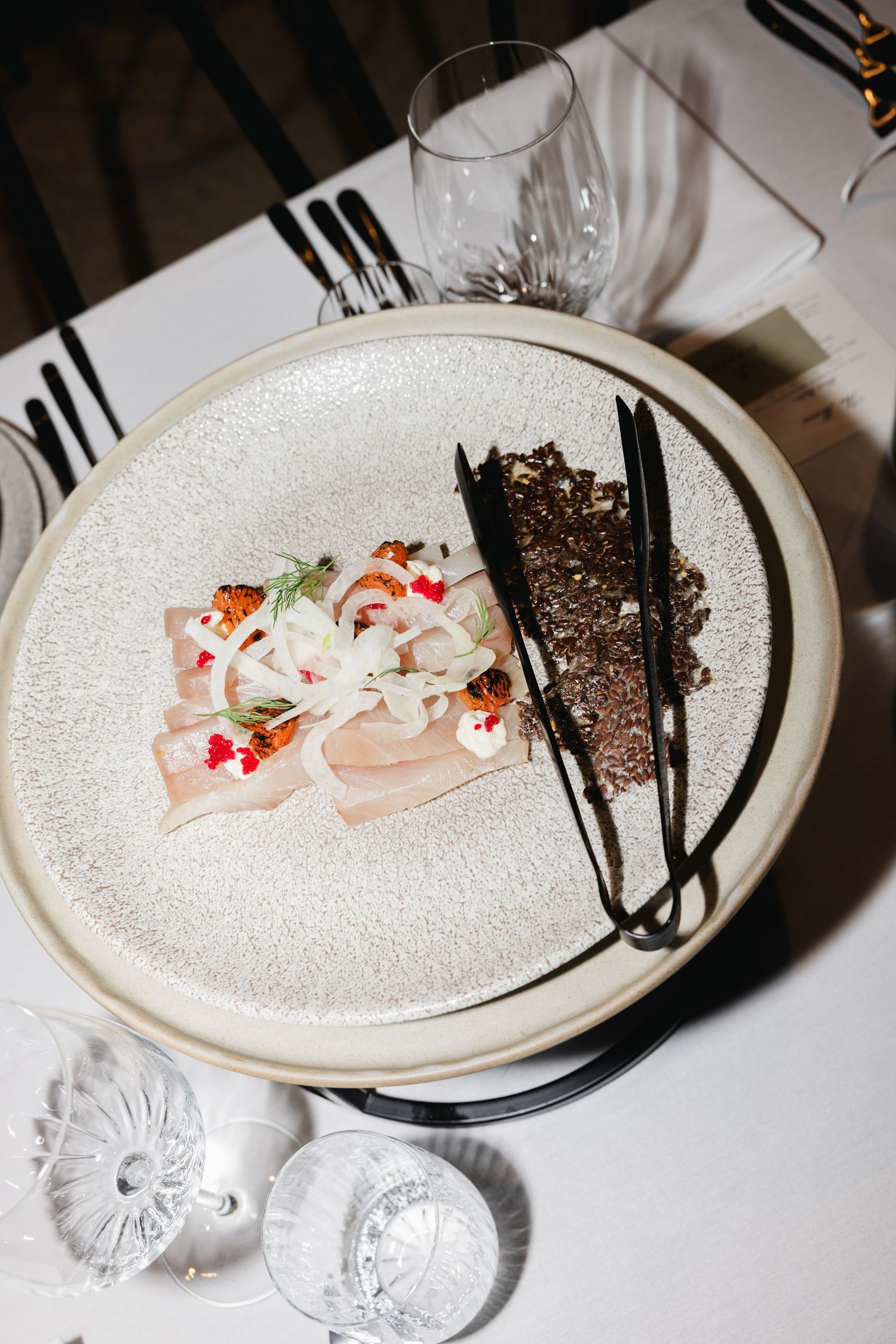 Elegant fine dining plate with cured fish, red caviar, onions, and dark rye bread on a textured white ceramic plate.