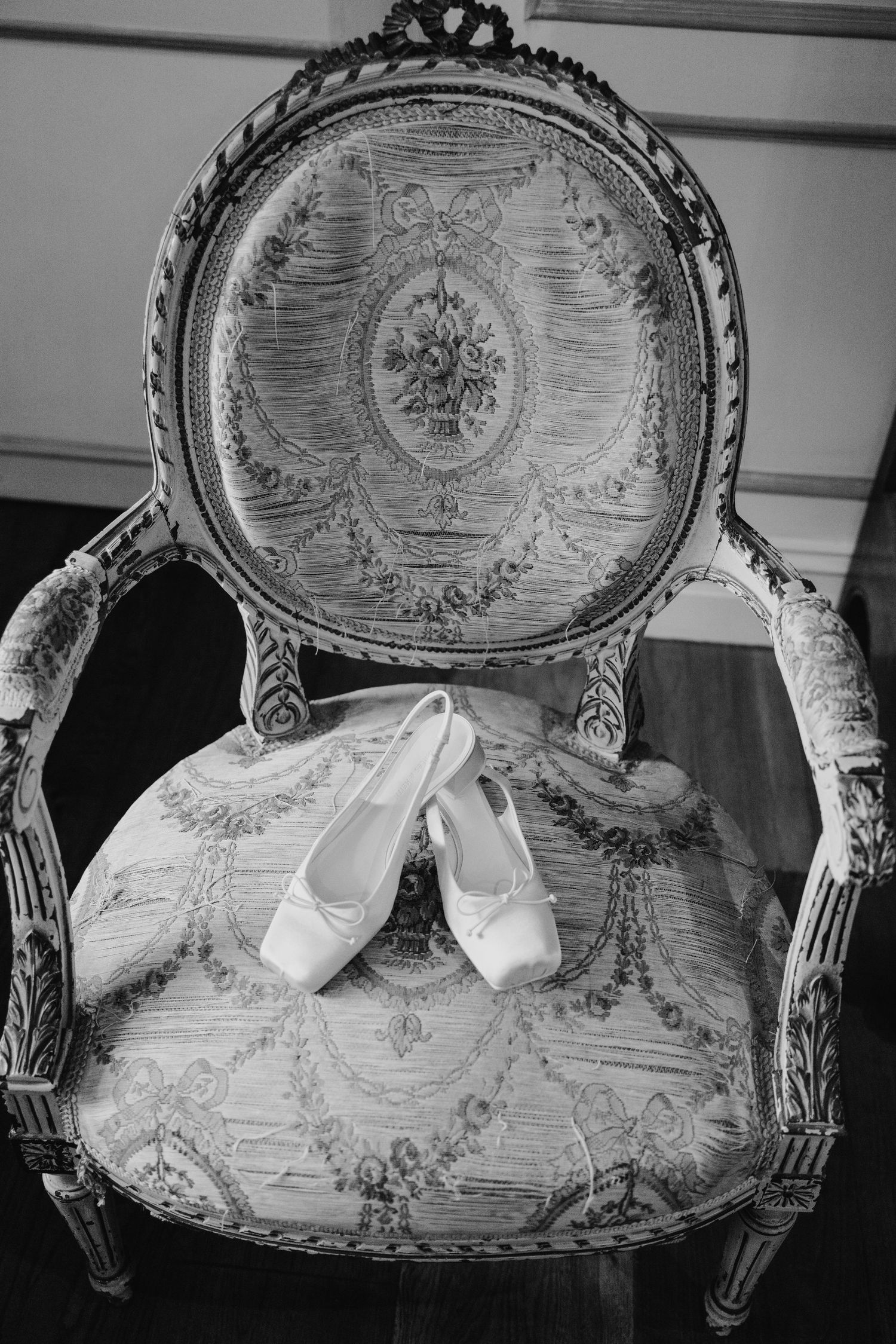 Elegant white bridal ballet flats resting on an ornate vintage French chair with floral tapestry upholstery.