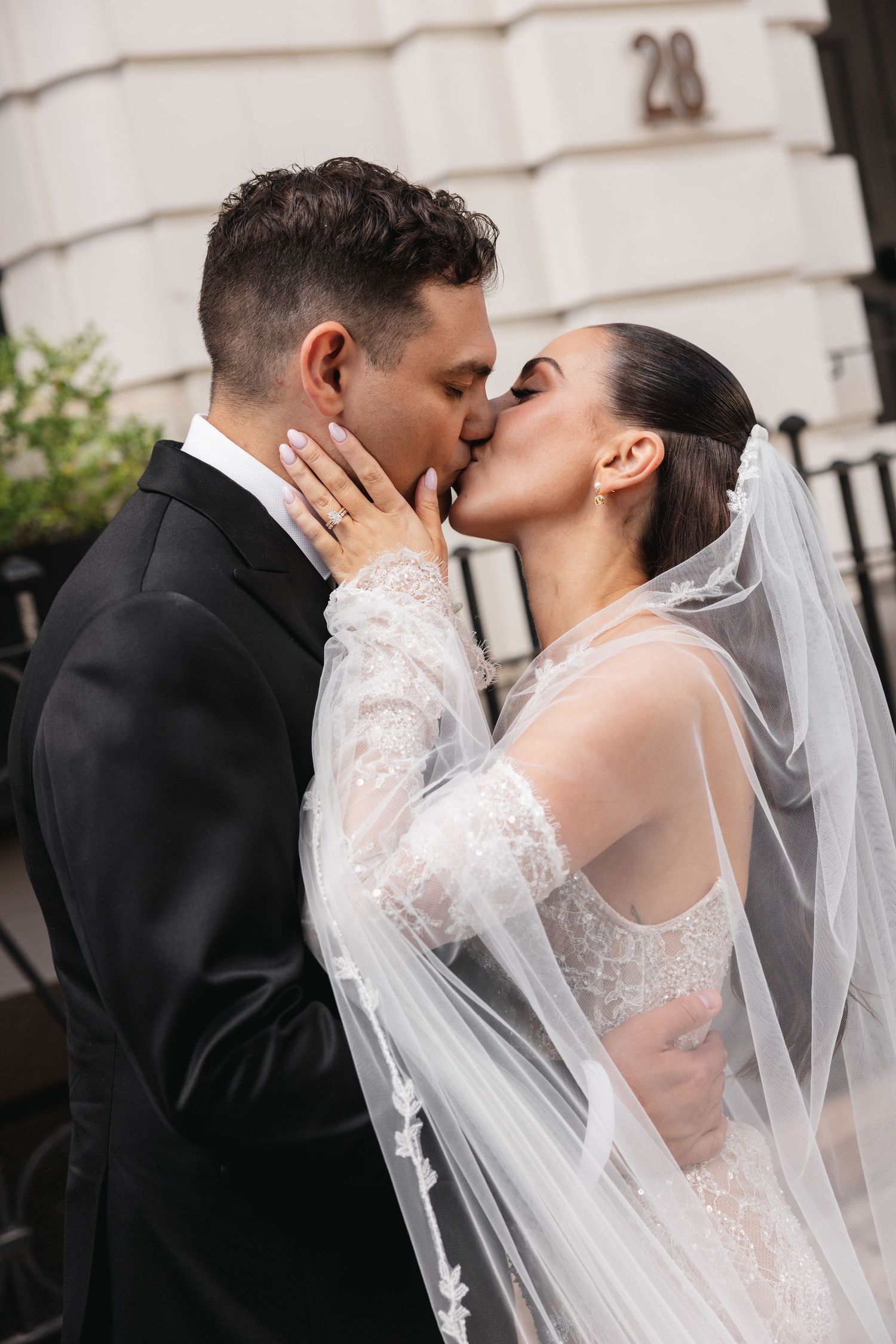 Bride and groom sharing a romantic kiss outdoors, bride wearing a lace dress and flowing veil.