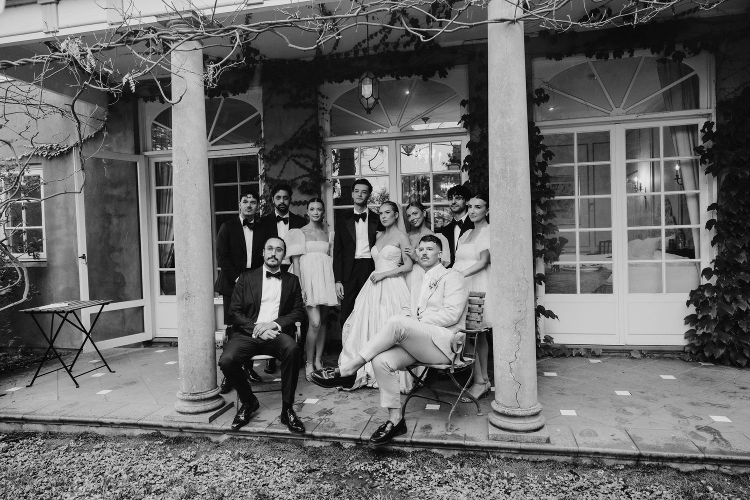 Black and white photo of a wedding party posing on a grand estate porch with columns.