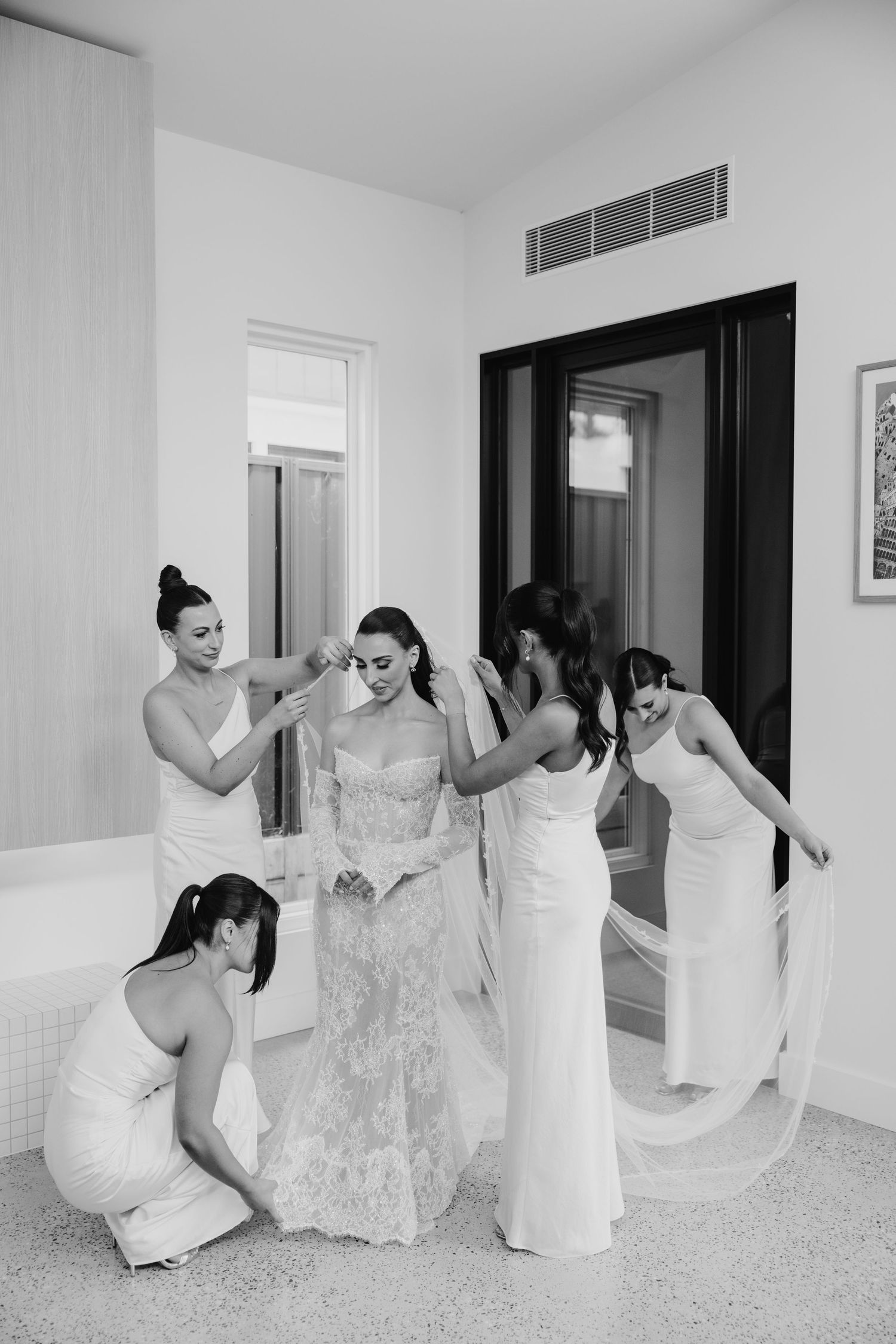Bridesmaids help bride with veil in elegant black and white wedding preparation photo.